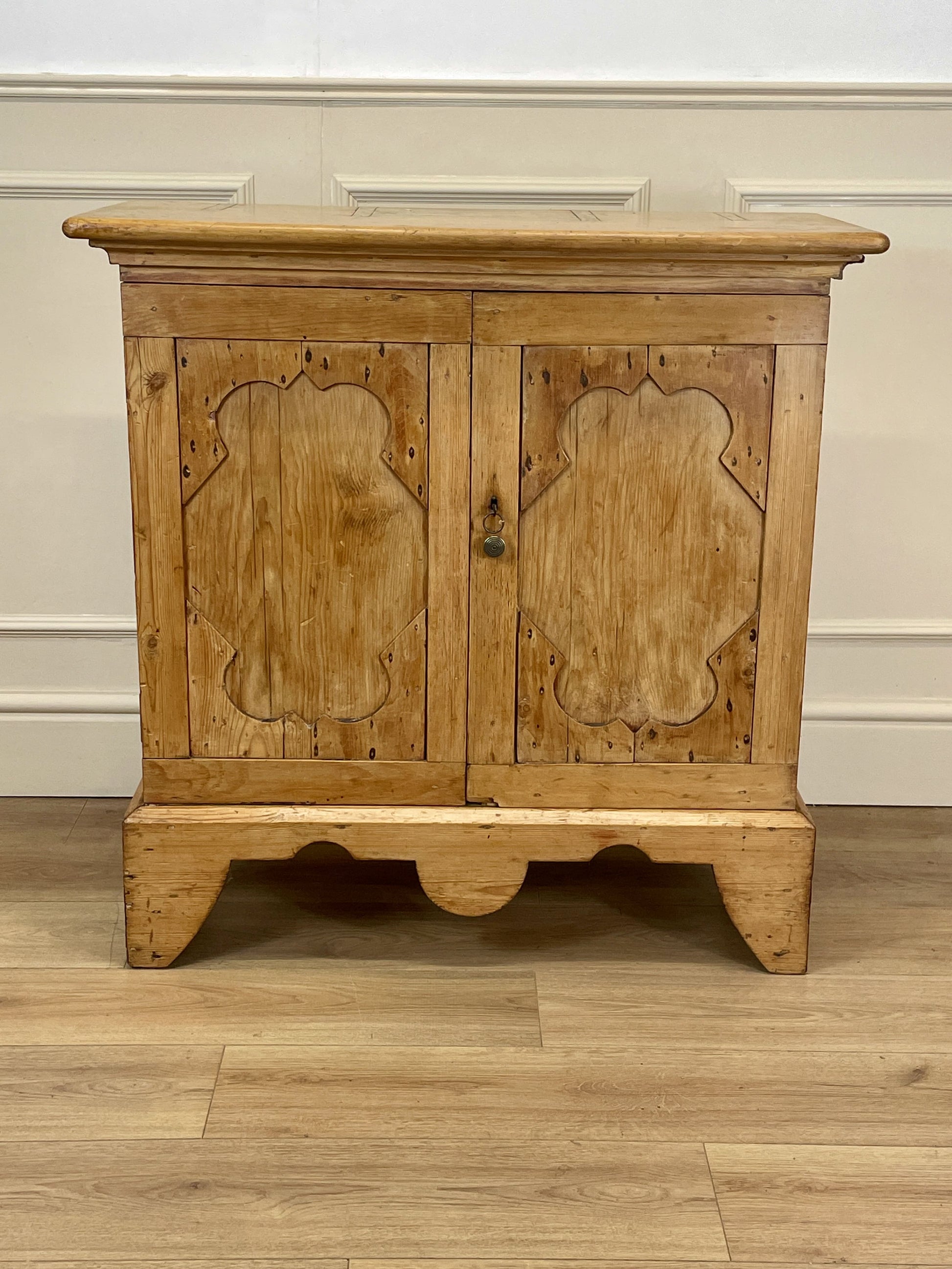 Wooden cabinet with carved doors on a wooden floor against a white wall.