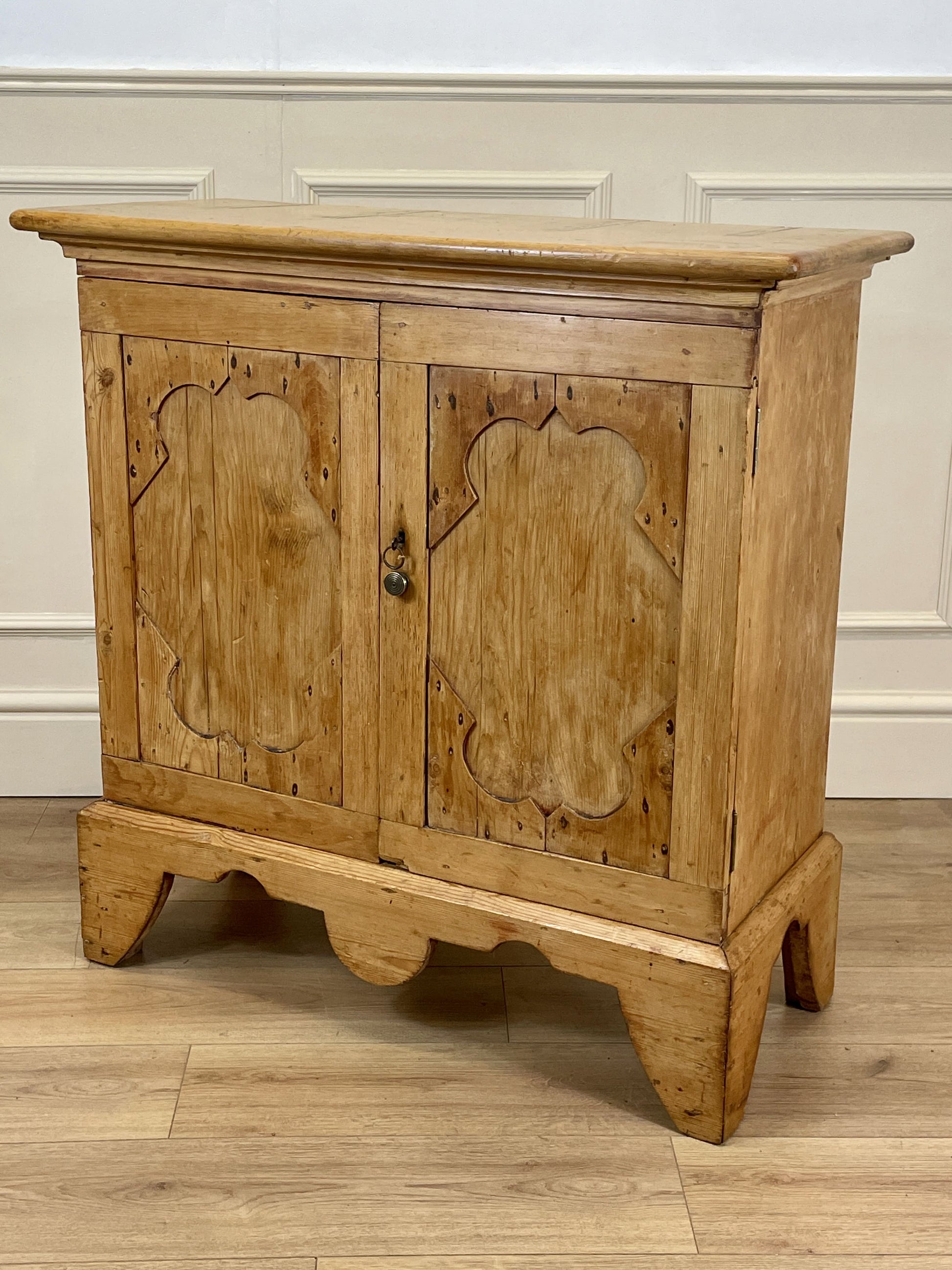 Wooden cabinet with carved doors on a wooden floor against a white wall.