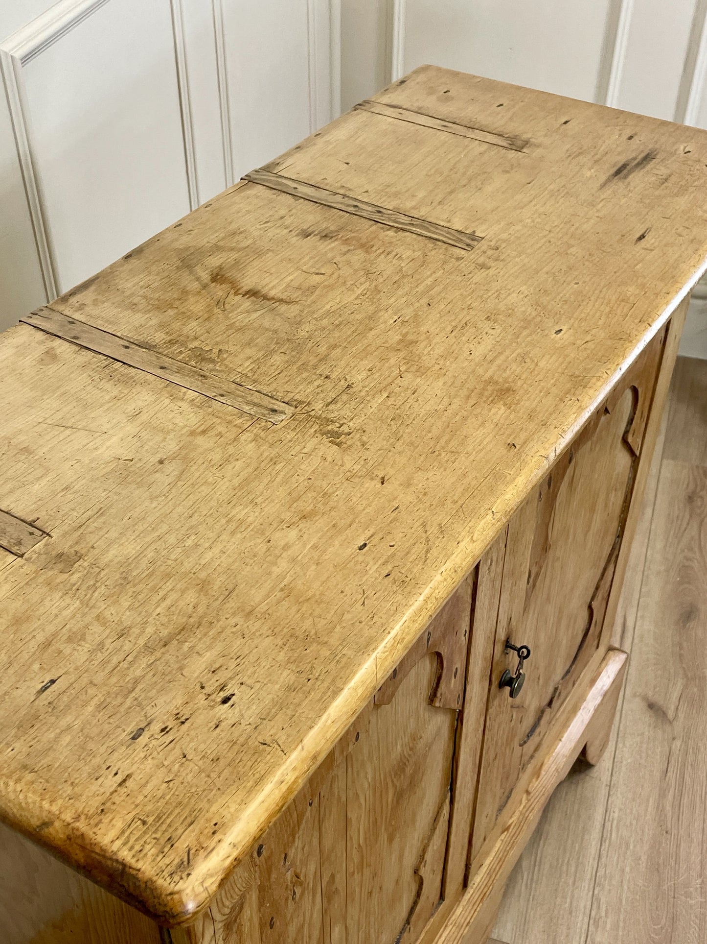 Vintage wooden dresser with a worn surface in a room with white paneling.