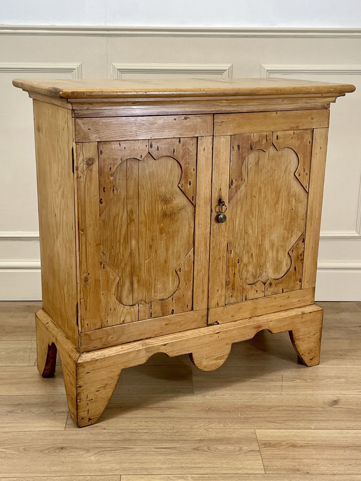 Wooden cabinet with carved doors on a wooden floor against a white wall.