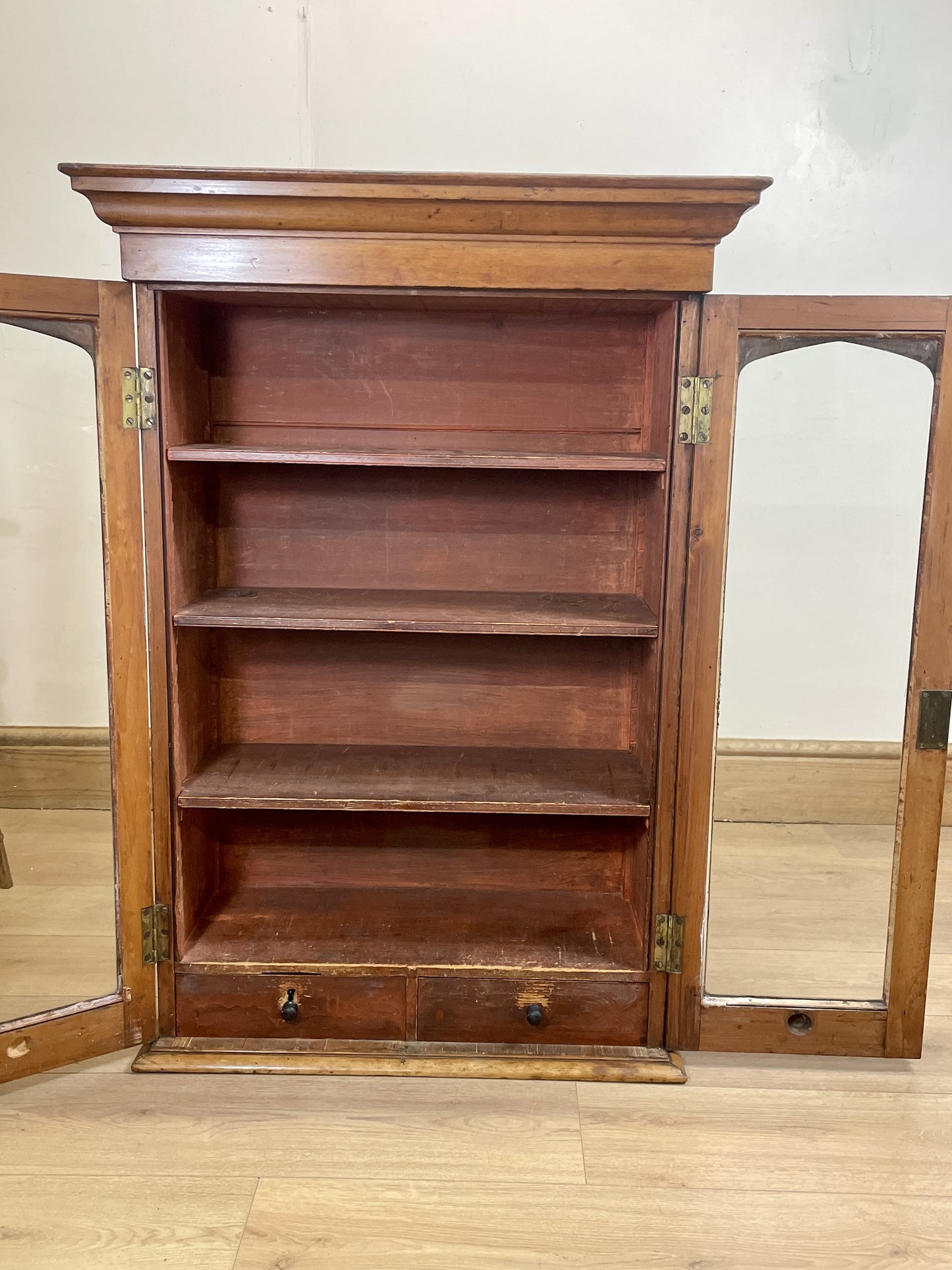Wooden bookshelf with mirrored doors on a wooden floor.