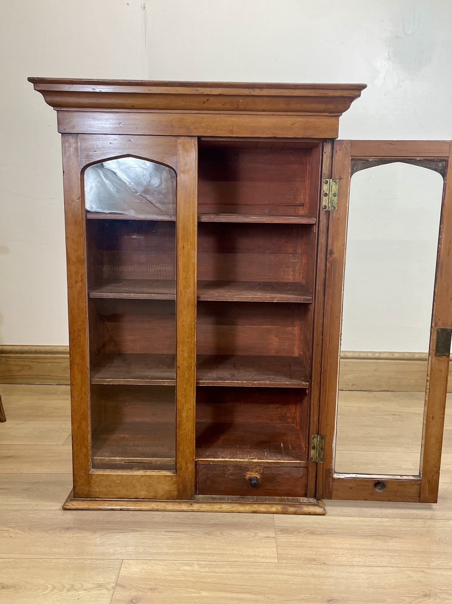 Wooden bookshelf with glass doors on a wooden floor.