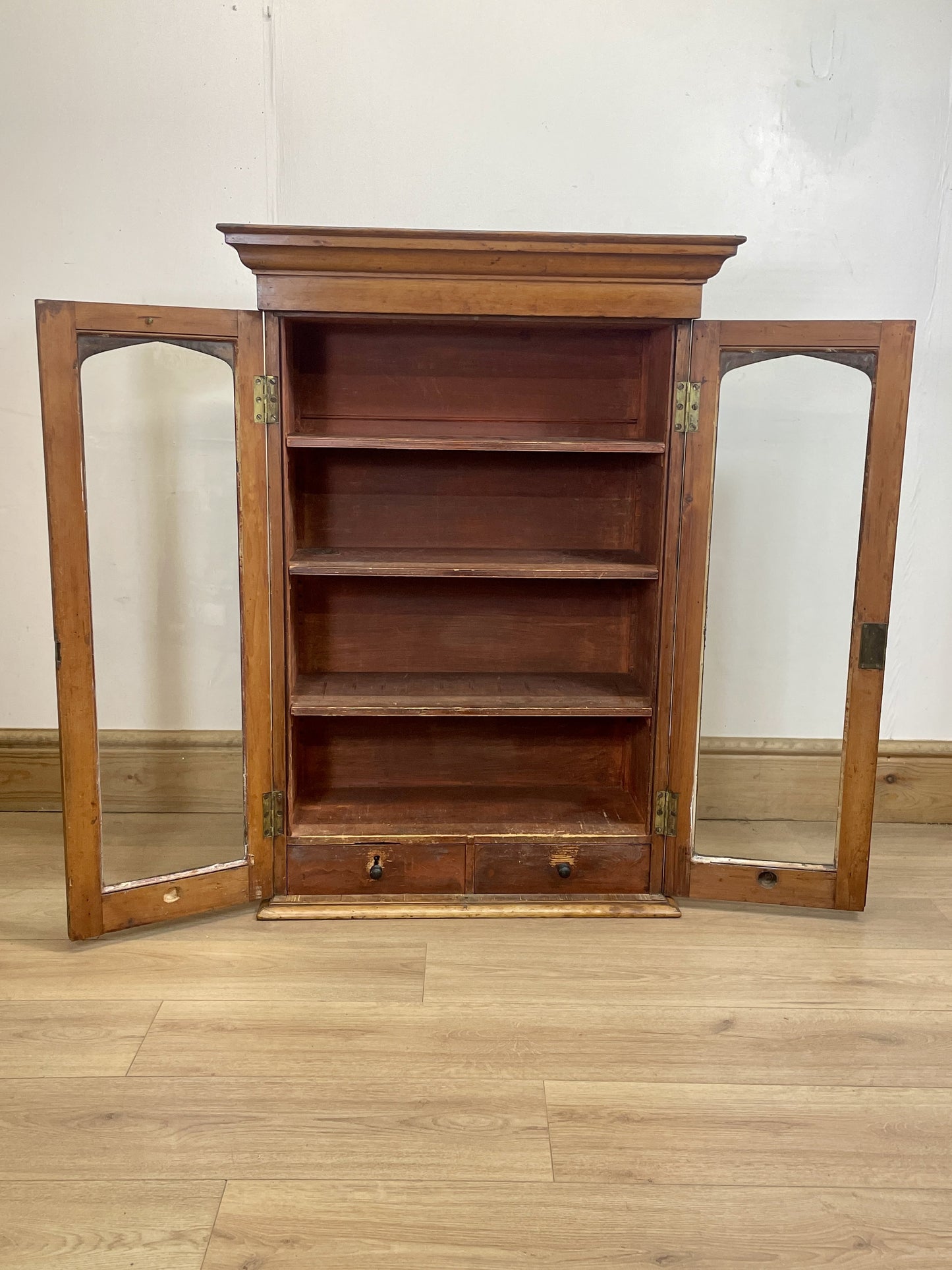 Wooden bookshelf with mirrored doors on a wooden floor.