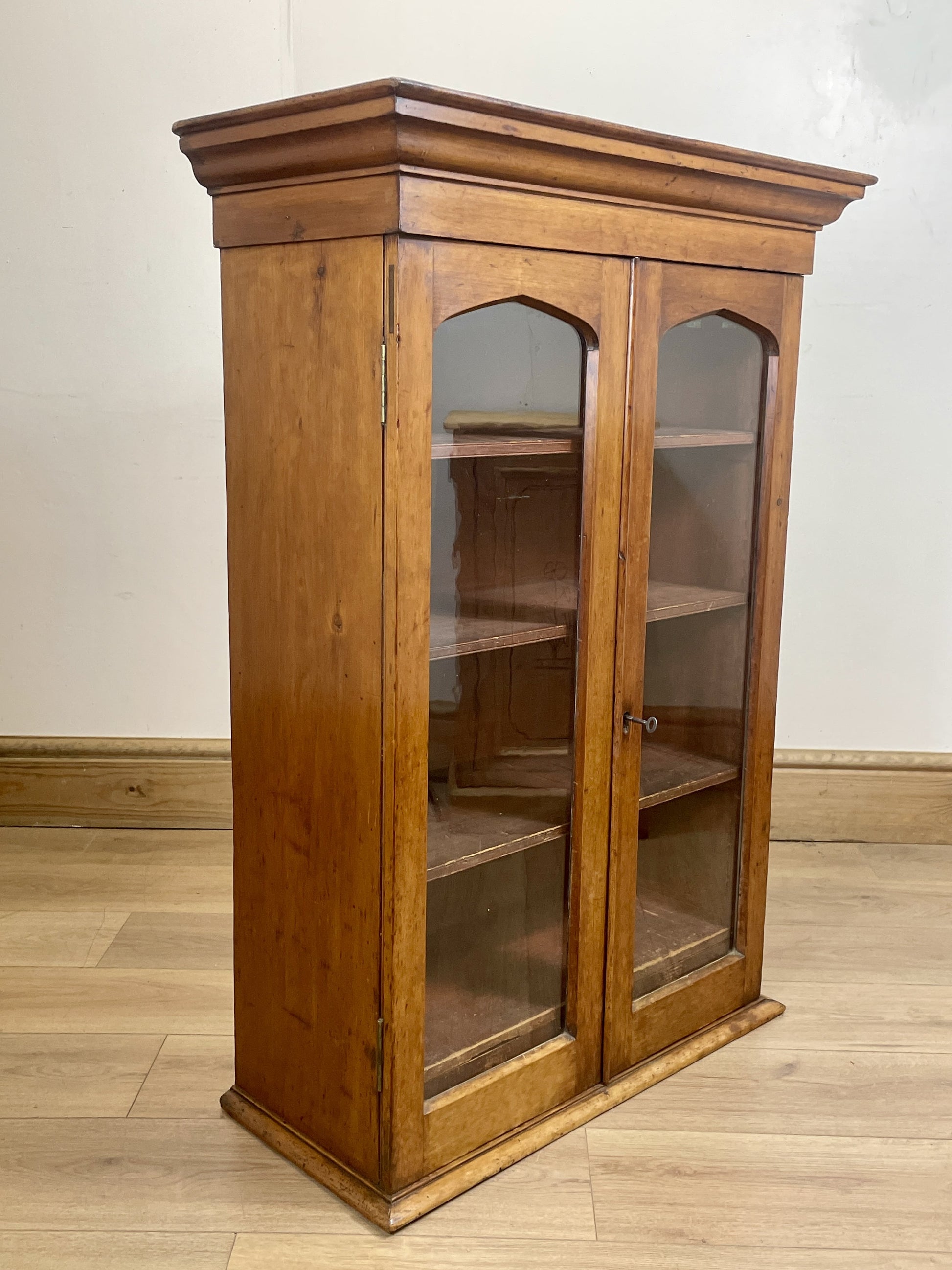Wooden display cabinet with glass doors on a wooden floor.