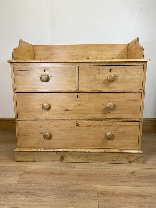 Wooden dresser with four drawers on a wooden floor against a white wall