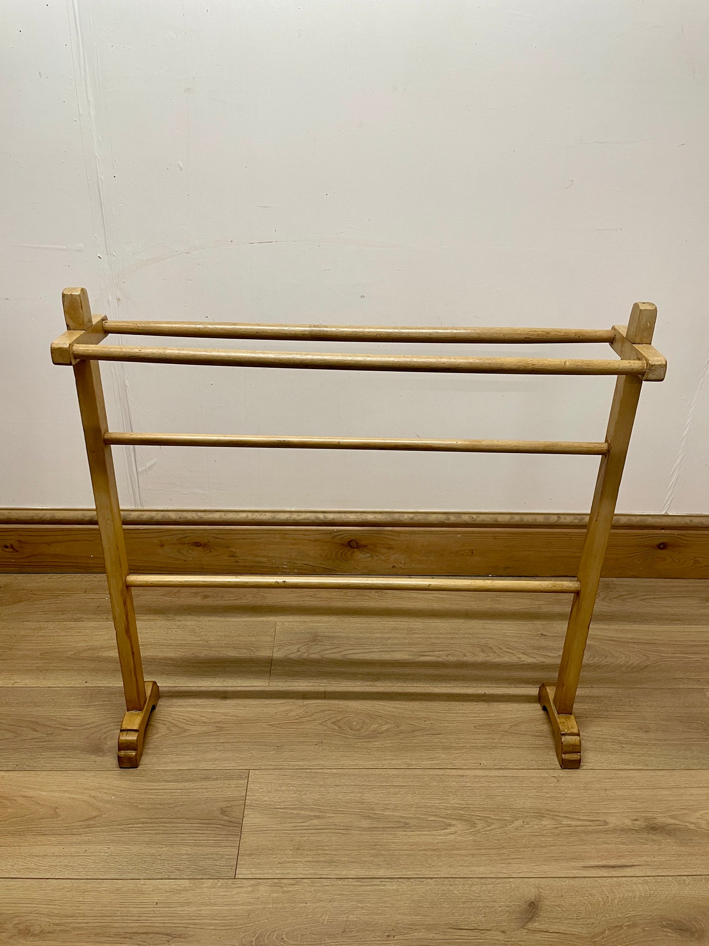 Wooden towel rack on a wooden floor with a white wall background