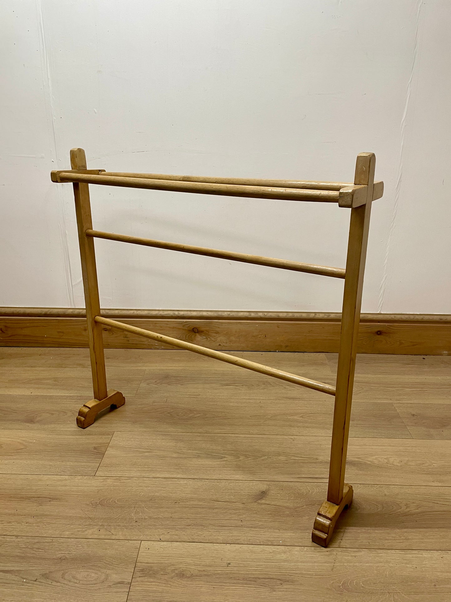 Wooden towel rack on a wooden floor with a white wall background
