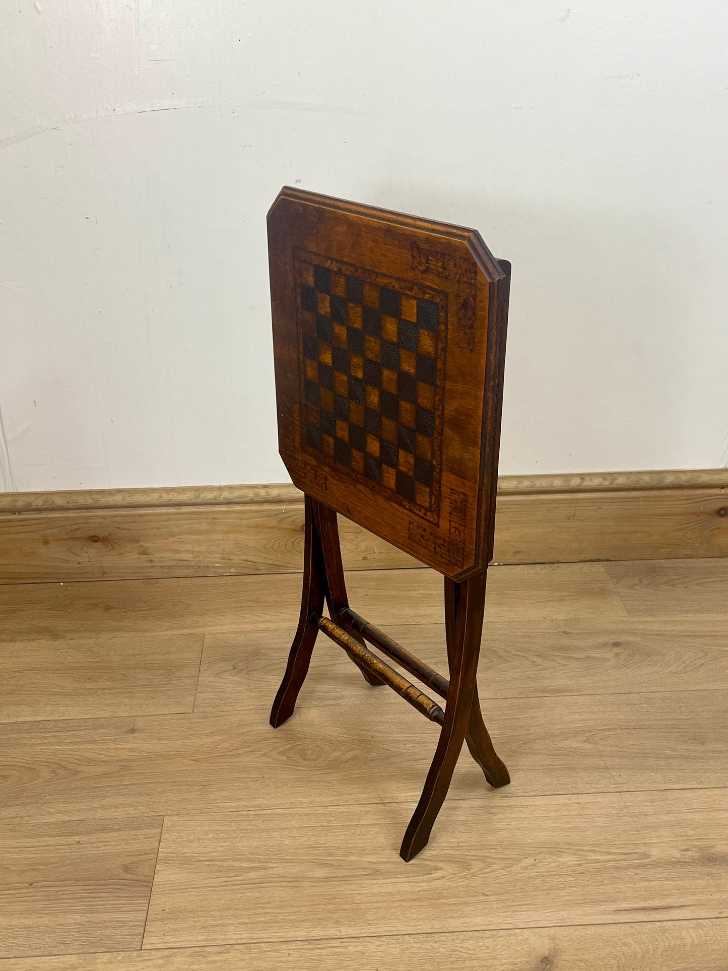 Wooden table with checkered surface on a wooden floor against a white wall