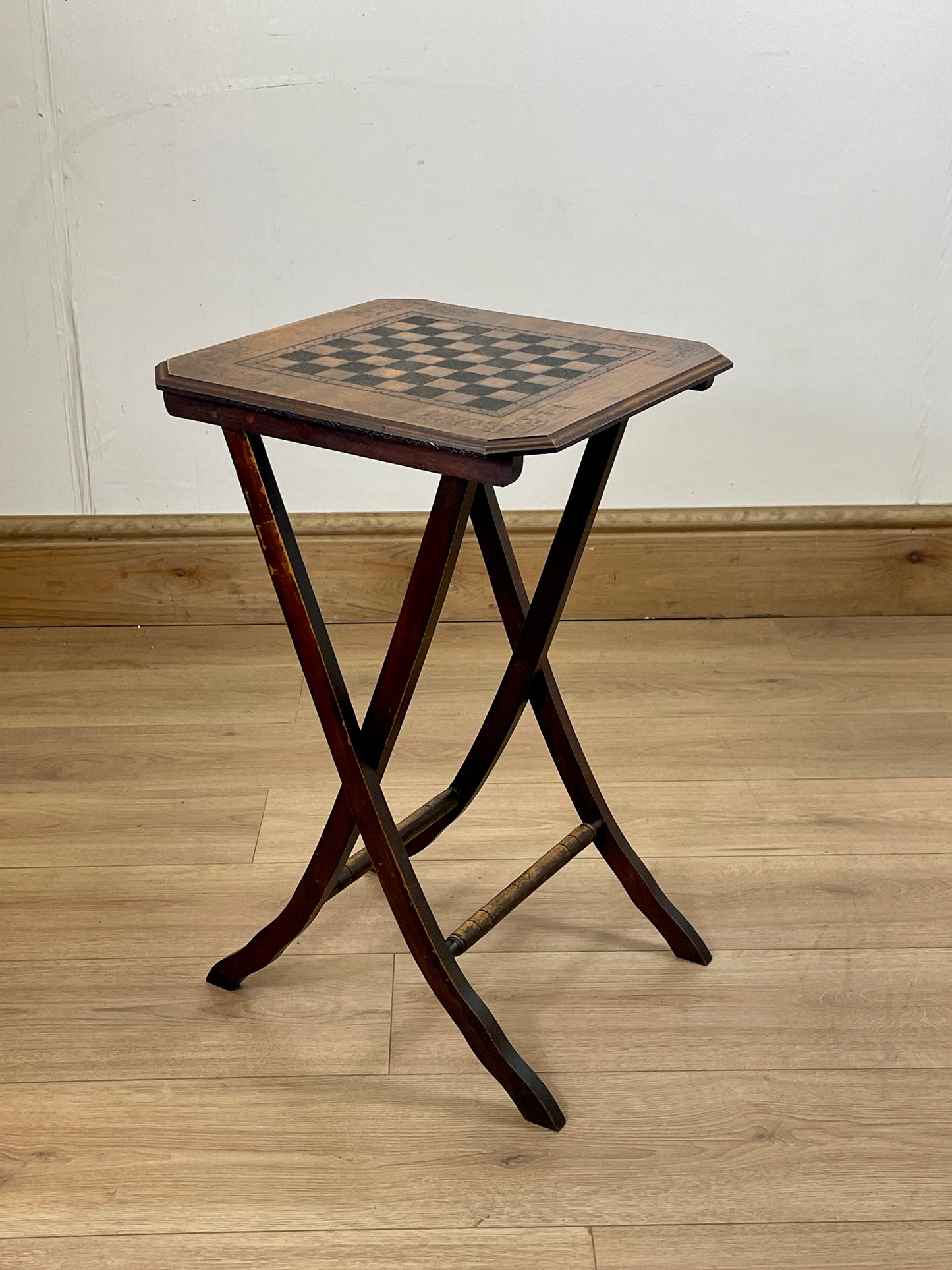 Wooden folding stool with checkered top on a wooden floor.
