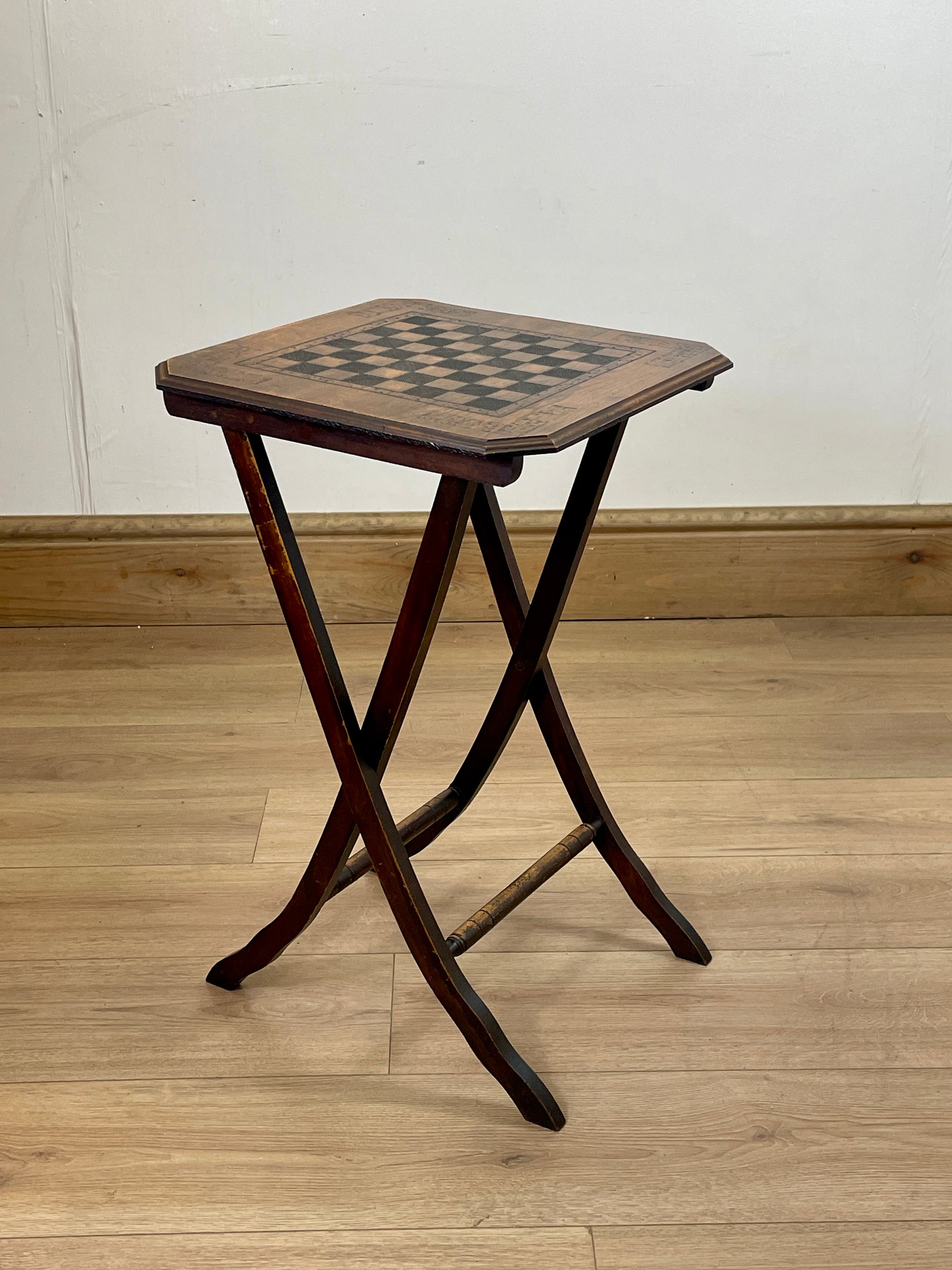 Wooden folding stool with checkered top on a wooden floor.