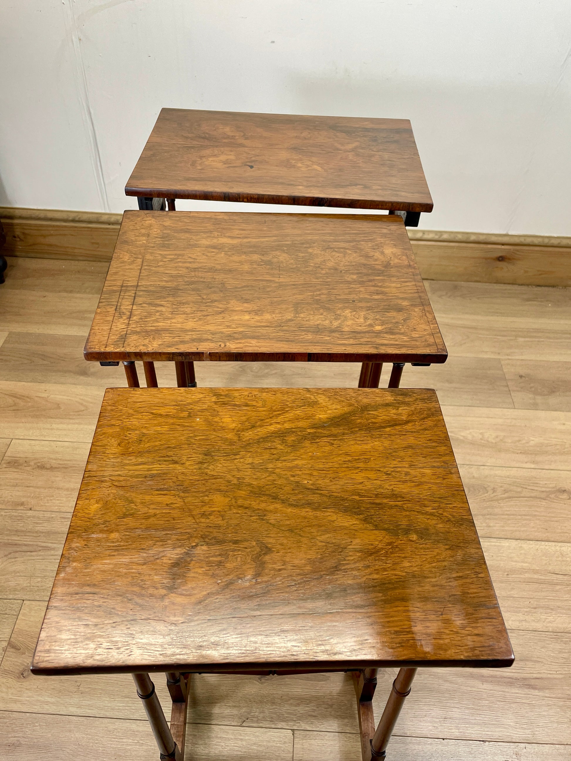 Three wooden nesting tables on a wooden floor with a white wall background