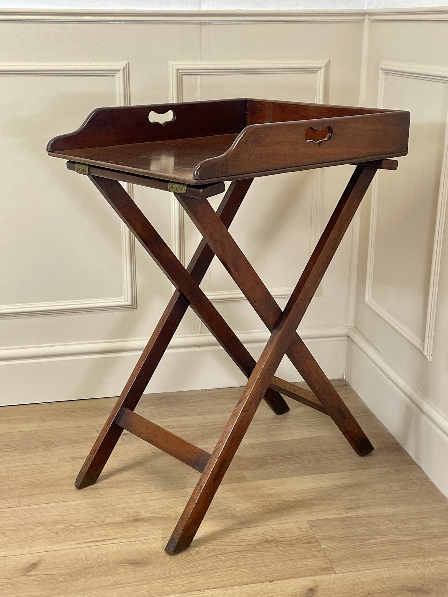 Wooden tray table with a tray on a wooden floor against a white paneled wall.