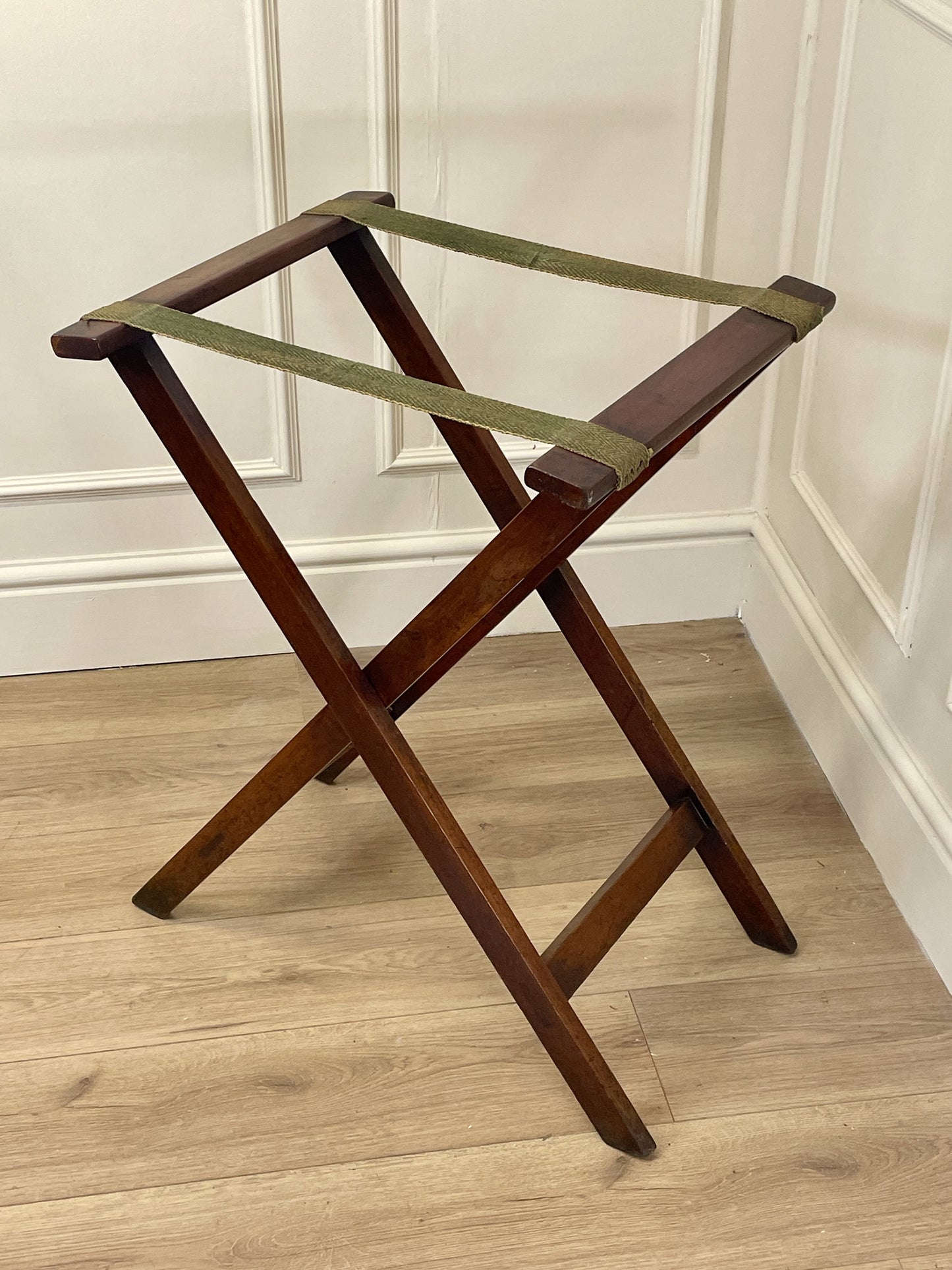 Wooden luggage rack with green straps on a wooden floor.