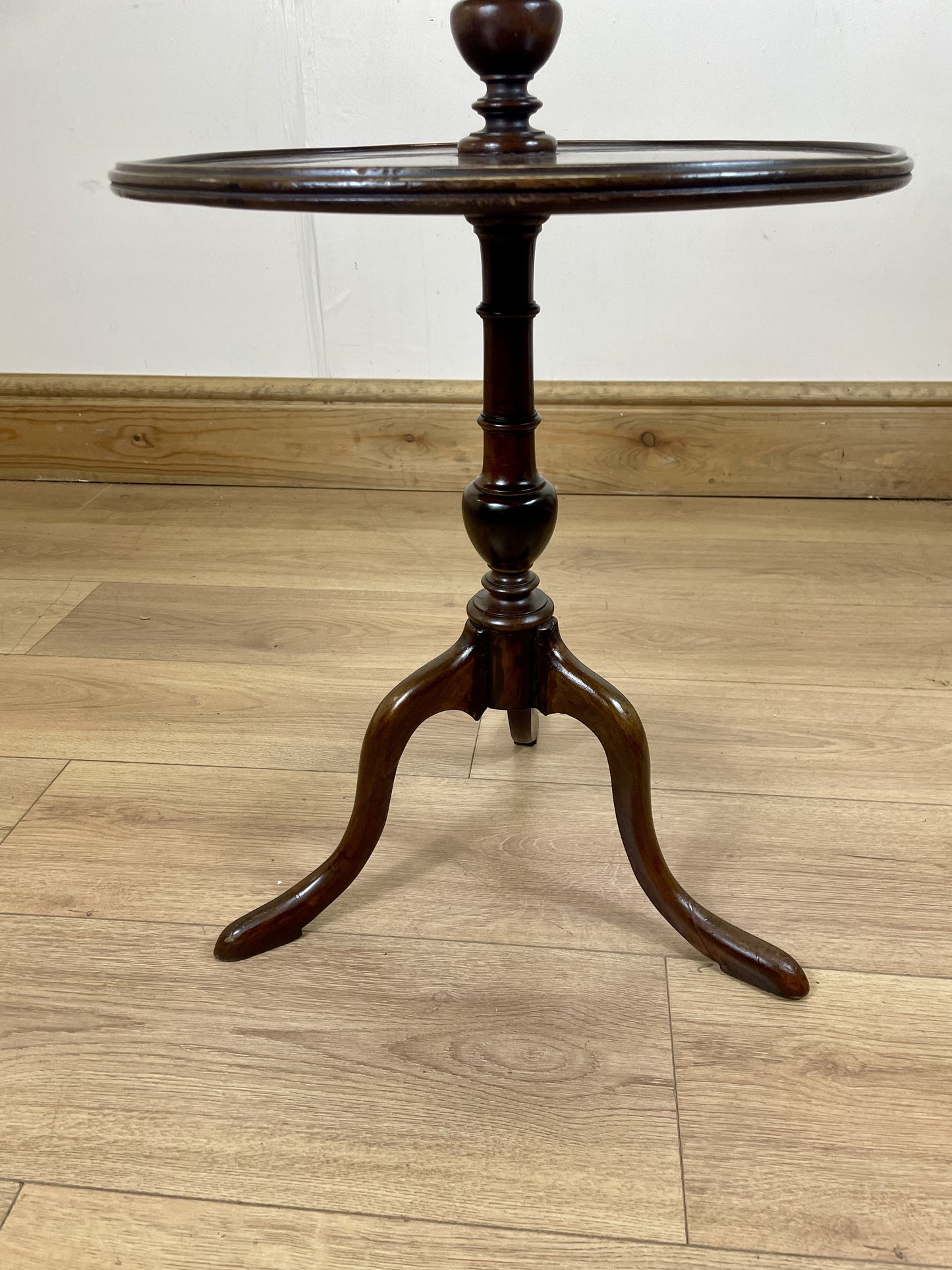 Wooden side table with a round top and three-legged base on a wooden floor.