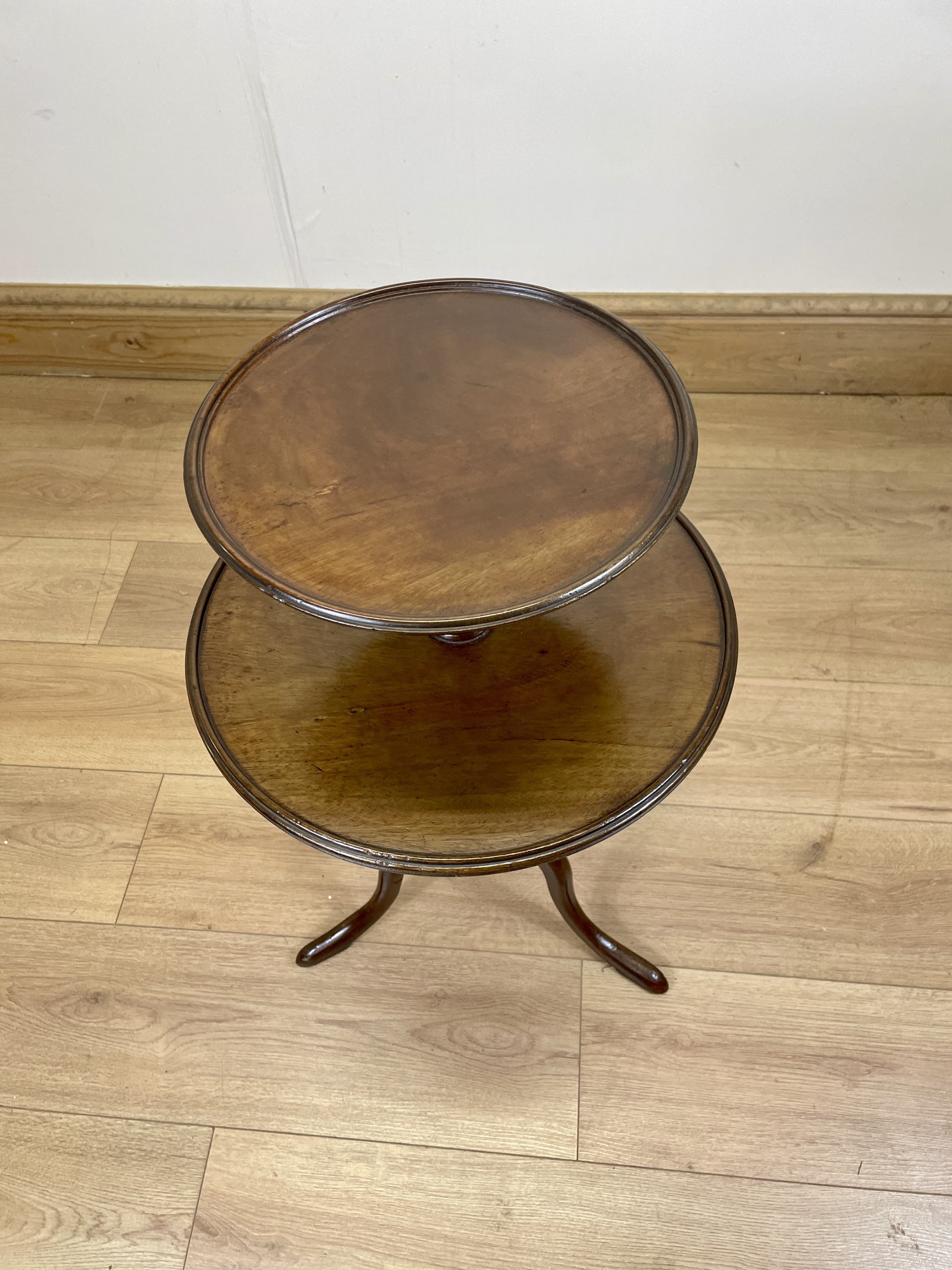 Two-tiered wooden side table on a wooden floor with a white wall background