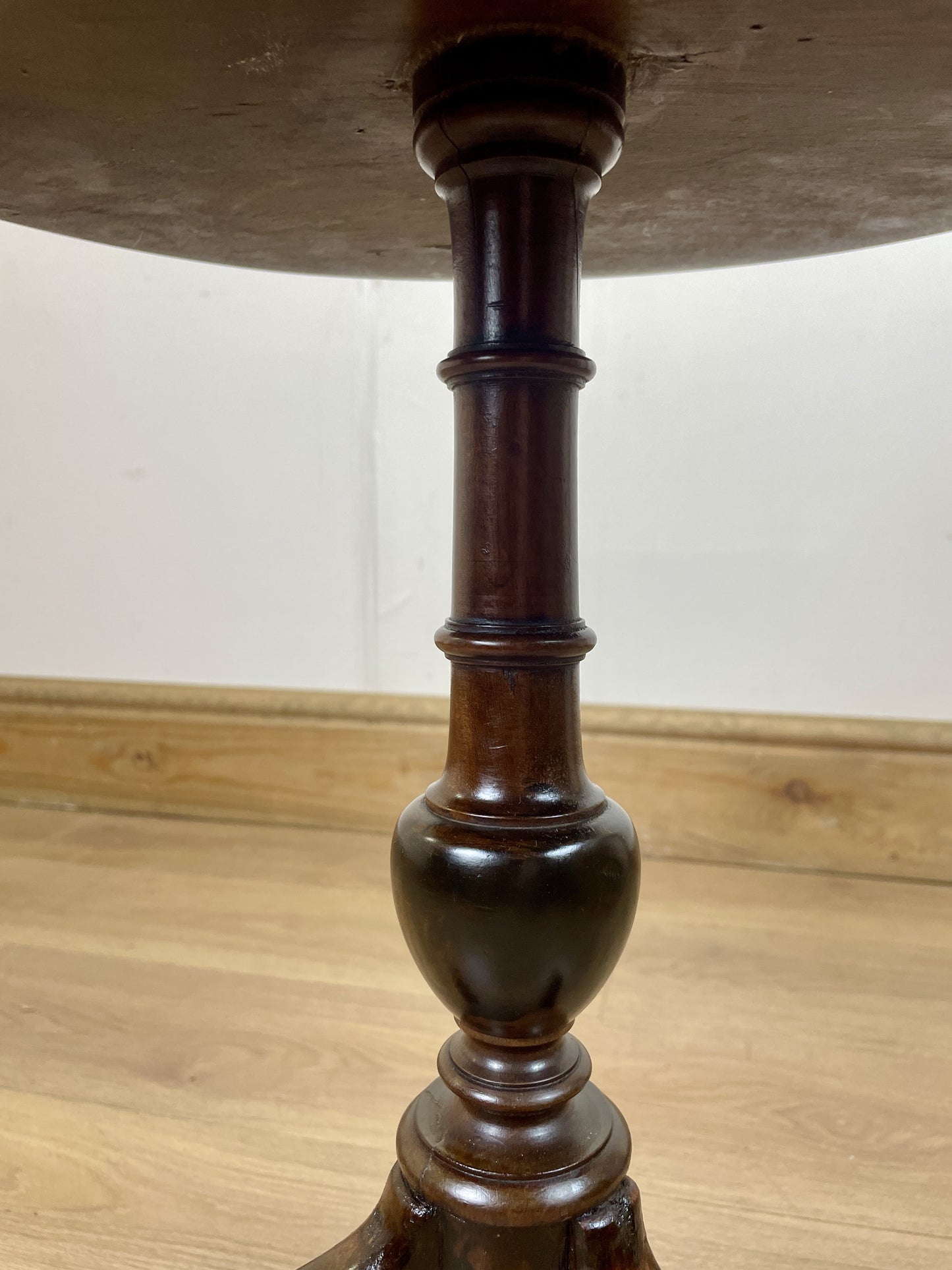Close-up of a wooden pedestal table leg on a wooden floor.