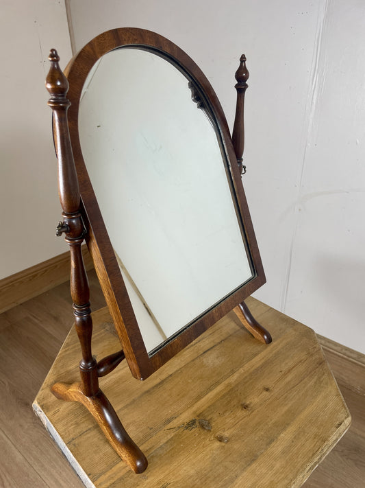 Wooden cheval mirror on a wooden stand against a white wall.