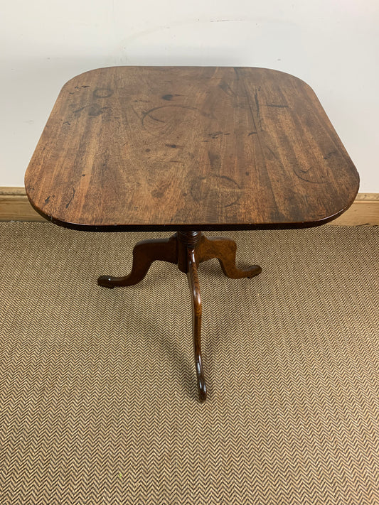 A Georgian style tilt-top table with a wooden surface and a tripod base, showing signs of age and use, indicative of historical craftsmanship.