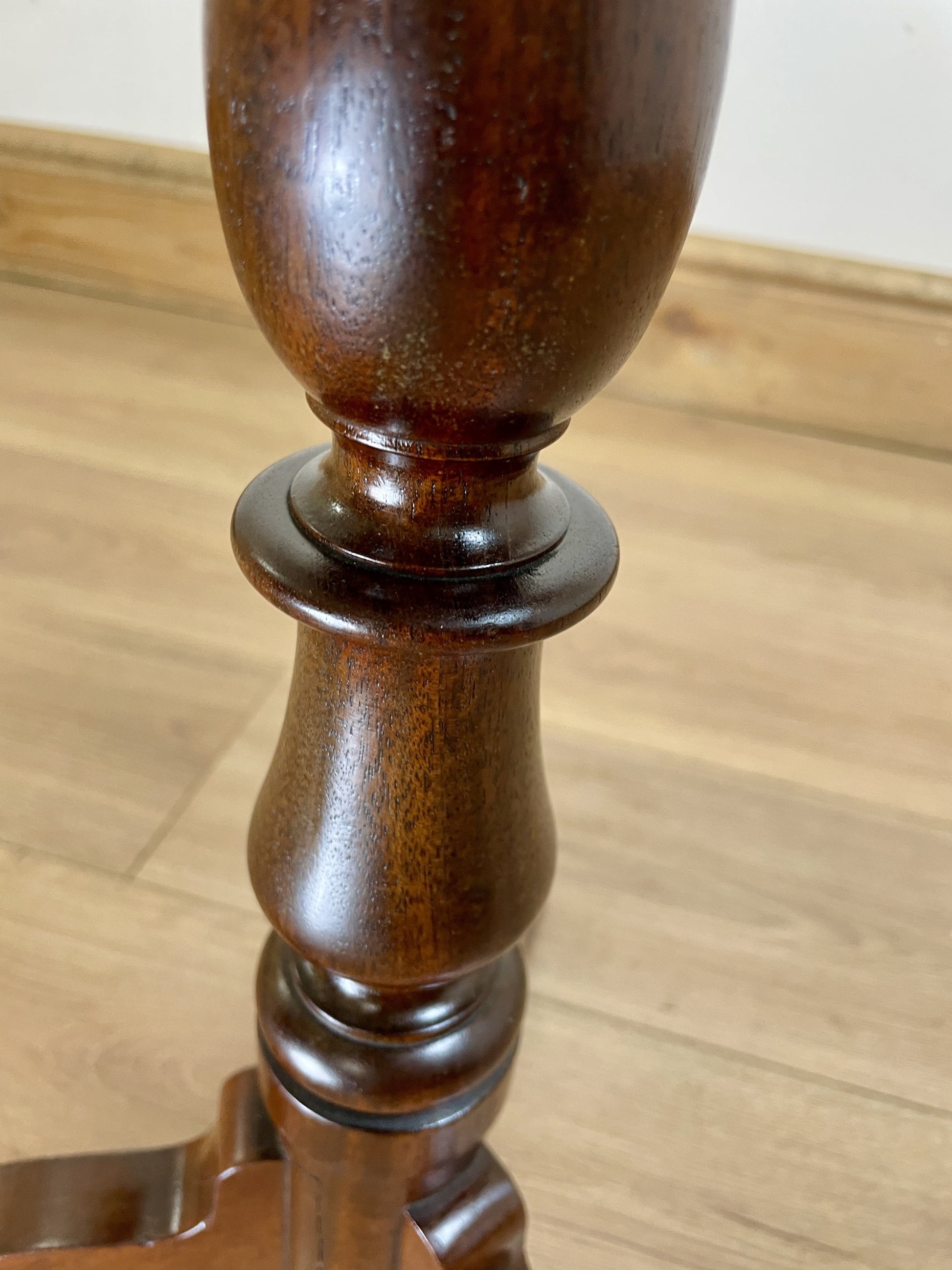 Close-up of a wooden leg on a piece of furniture with a light wood floor background.