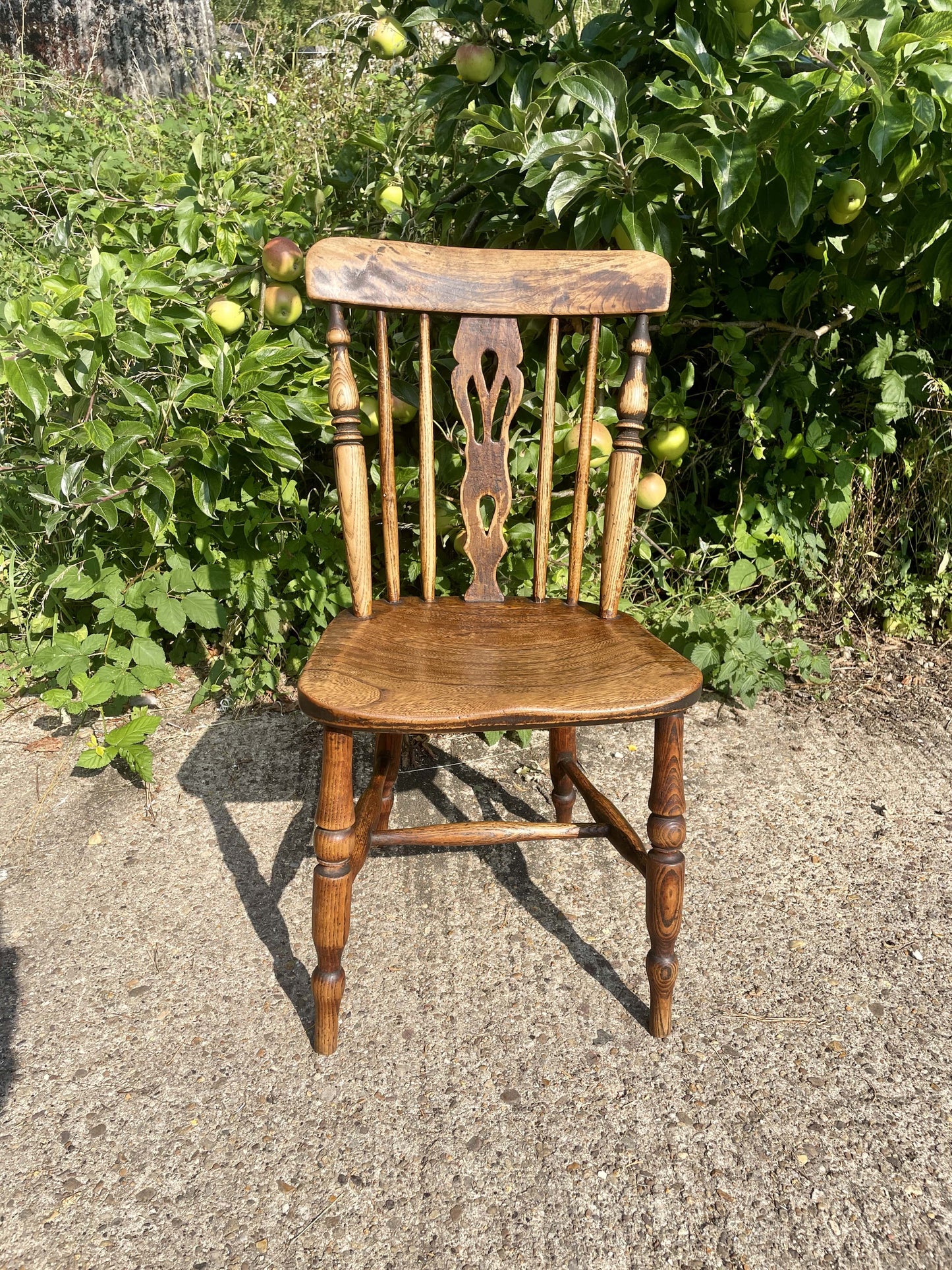 Wooden chair with a decorative backrest in an outdoor setting with greenery.