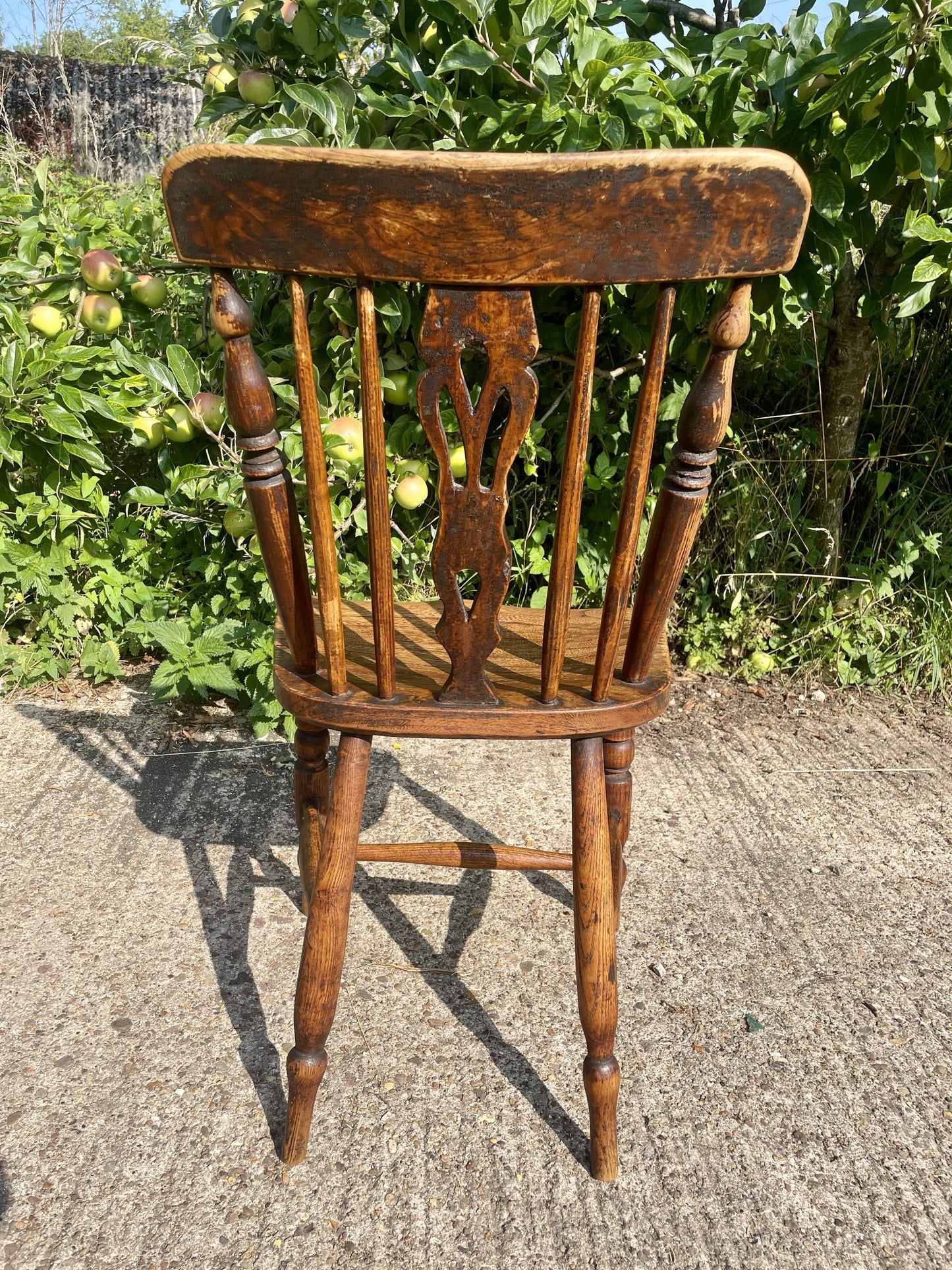 Wooden chair with a decorative backrest on a concrete surface with greenery in the background