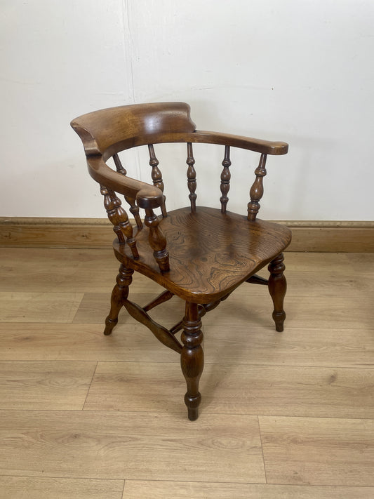 Wooden chair with curved armrests on a wooden floor against a white wall