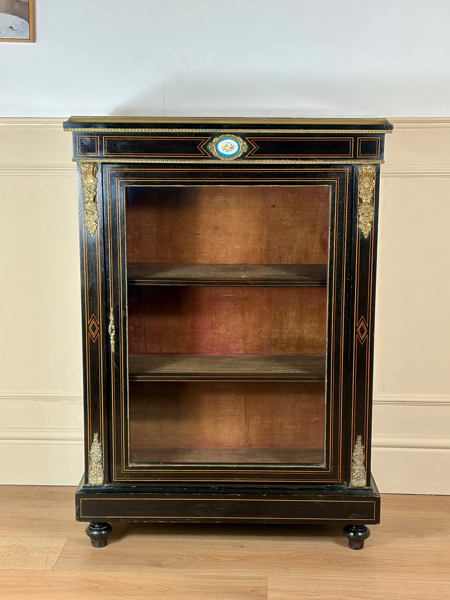 Decorative bookshelf with glass front against a white wall.