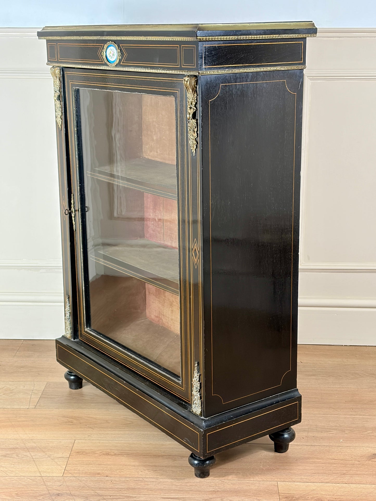 Decorative cabinet with glass door on a wooden floor against a white wall