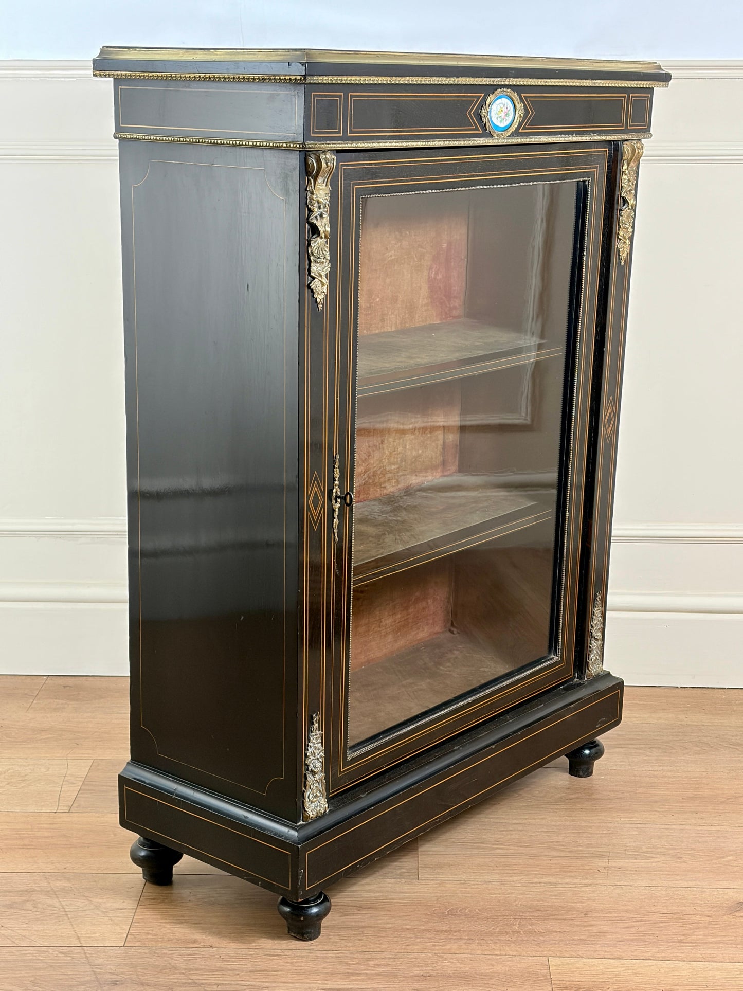 Decorative glass cabinet with black and gold finish on a wooden floor.