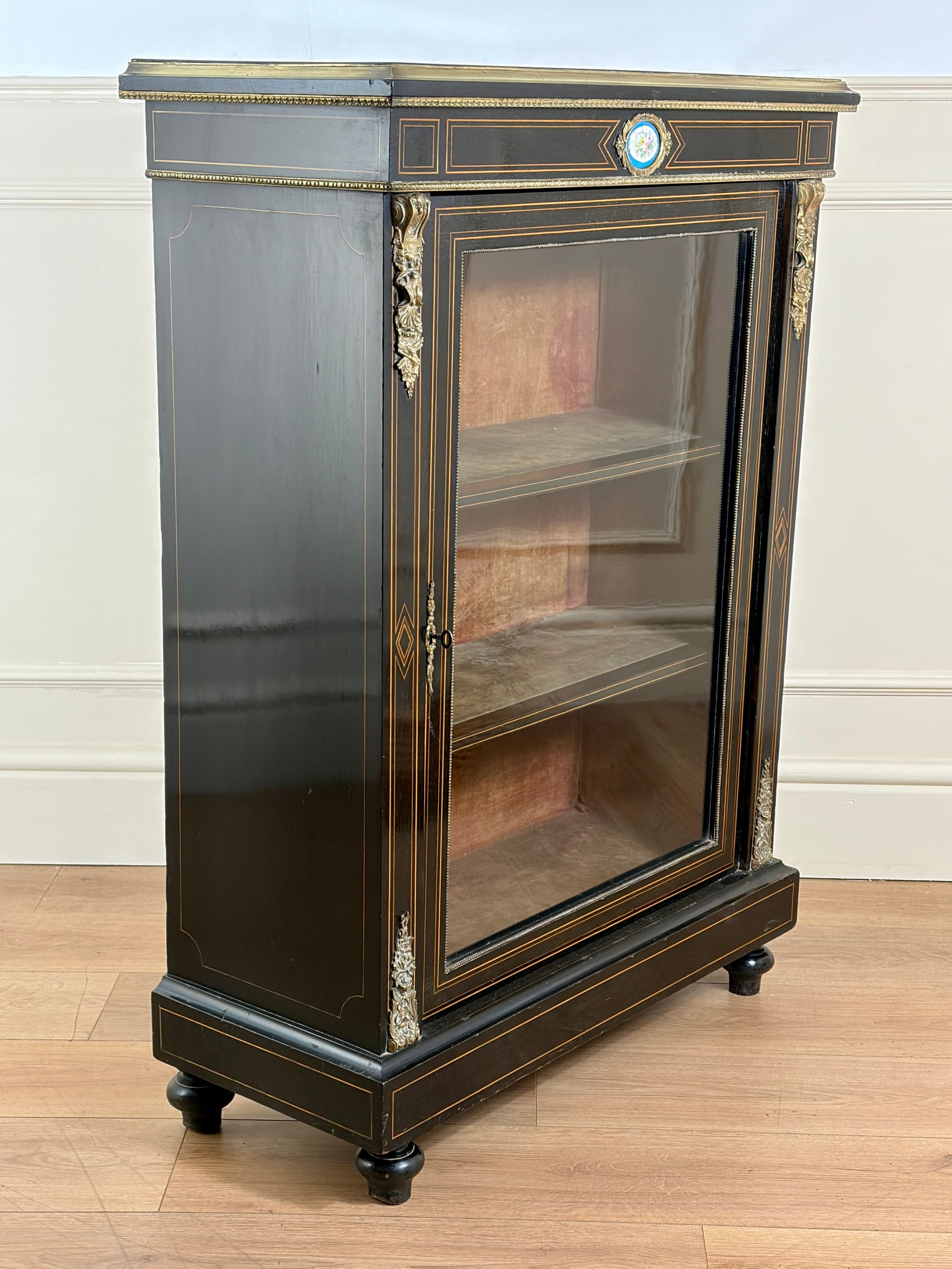 Decorative glass cabinet with black and gold finish on a wooden floor.
