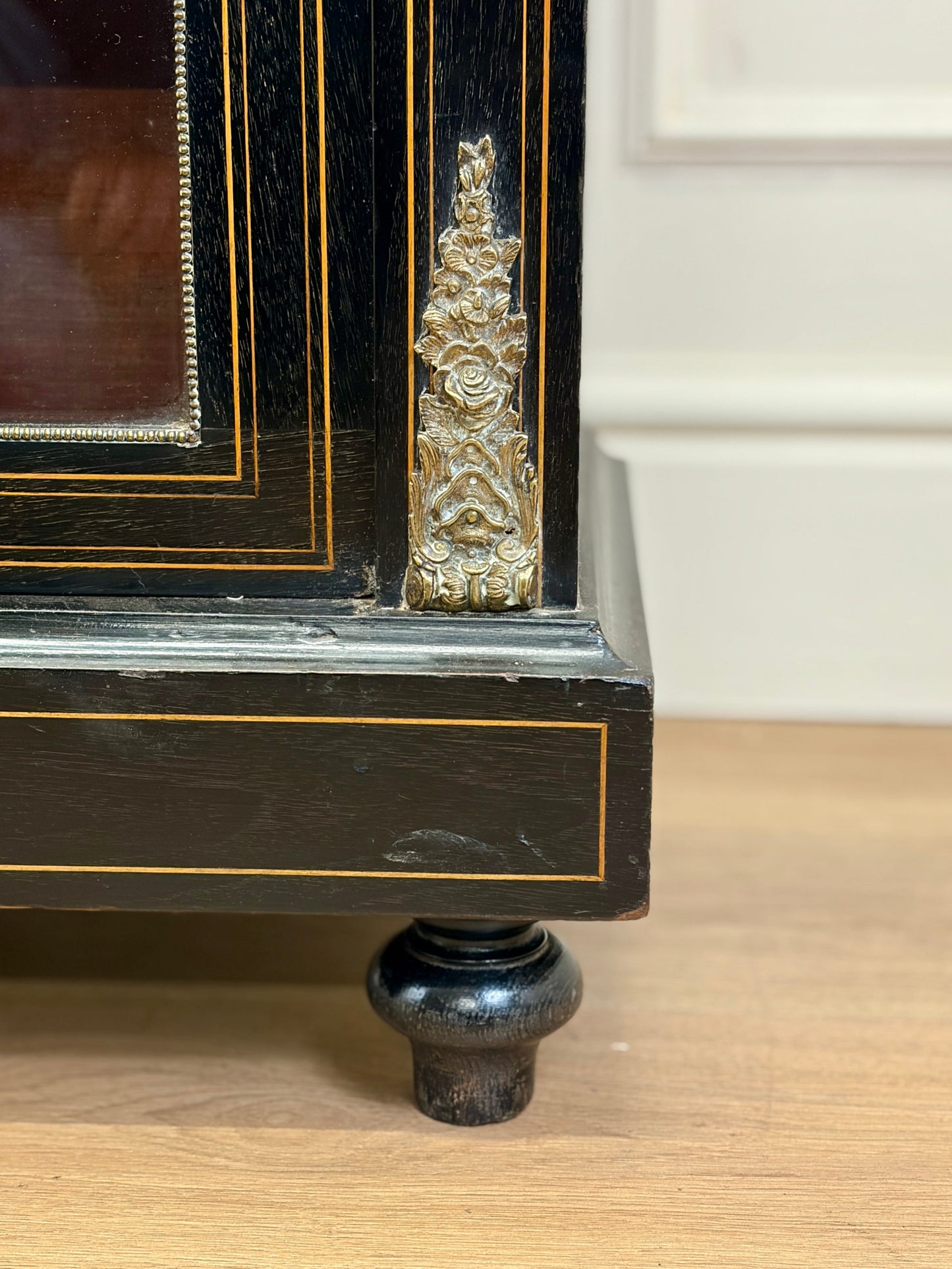 Close-up of a black wooden cabinet with gold accents on a wooden floor.
