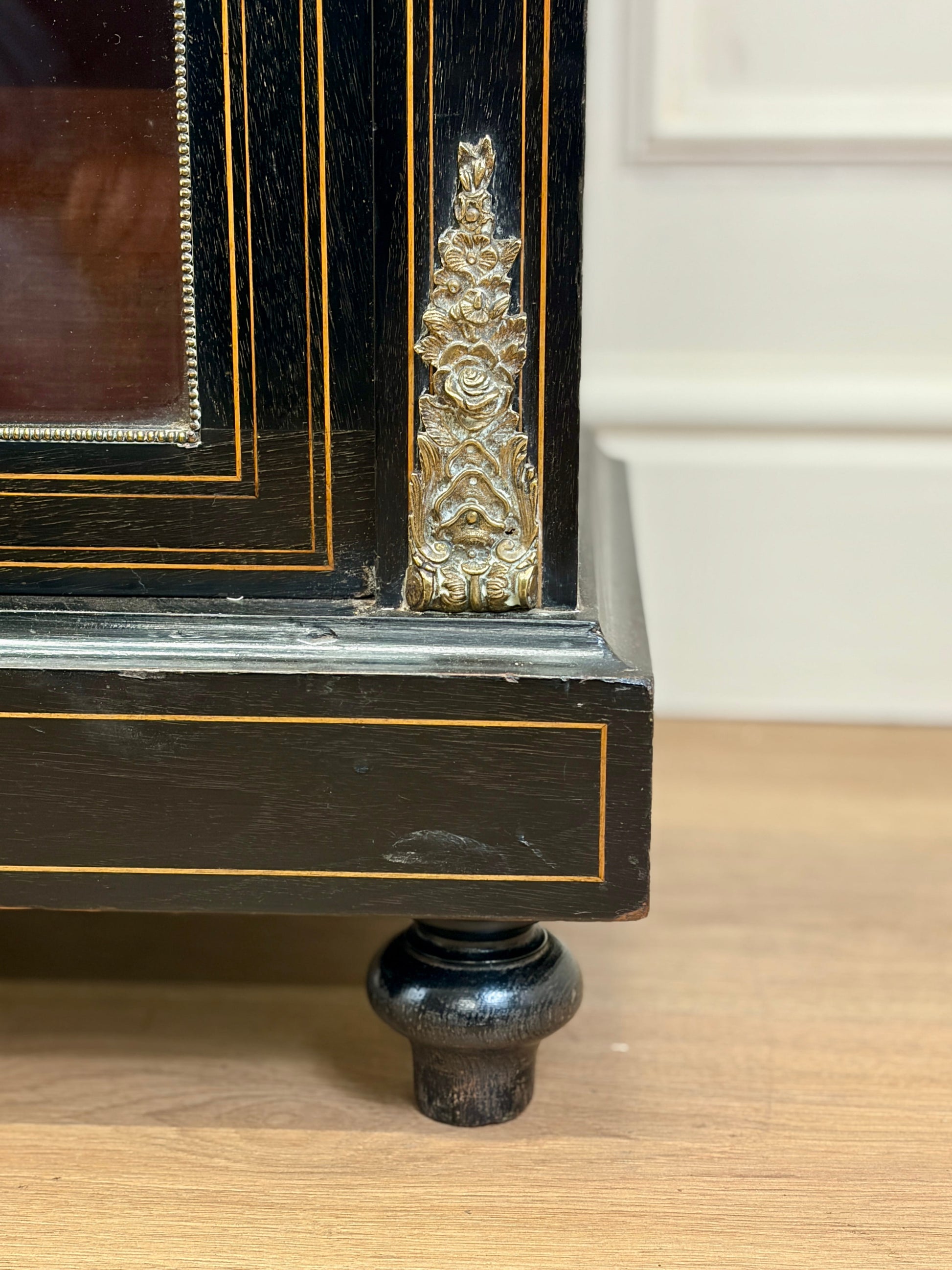 Close-up of a black wooden cabinet with gold accents on a wooden floor.