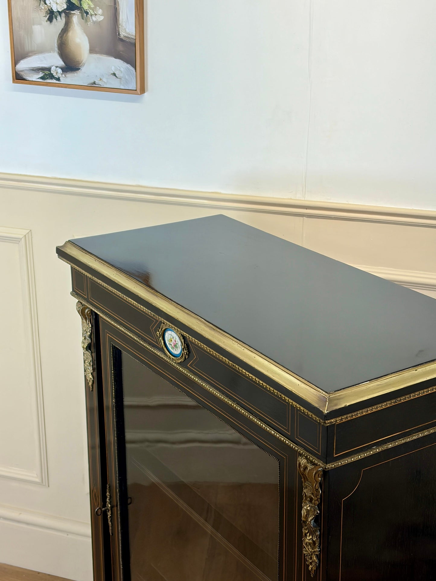 Decorative cabinet with gold accents in a room with white walls and a framed picture.