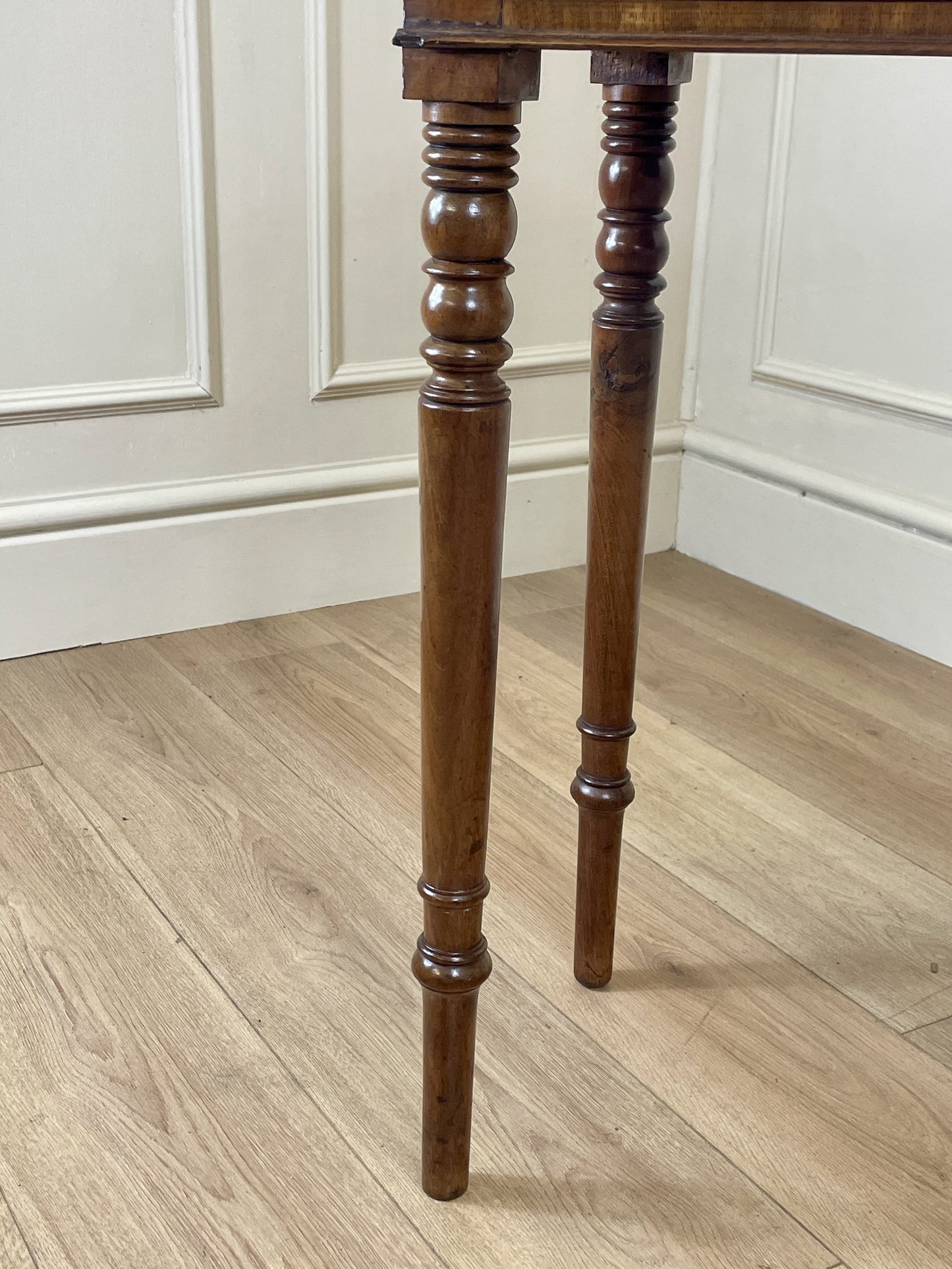 Wooden table legs on a wooden floor with white paneled walls.