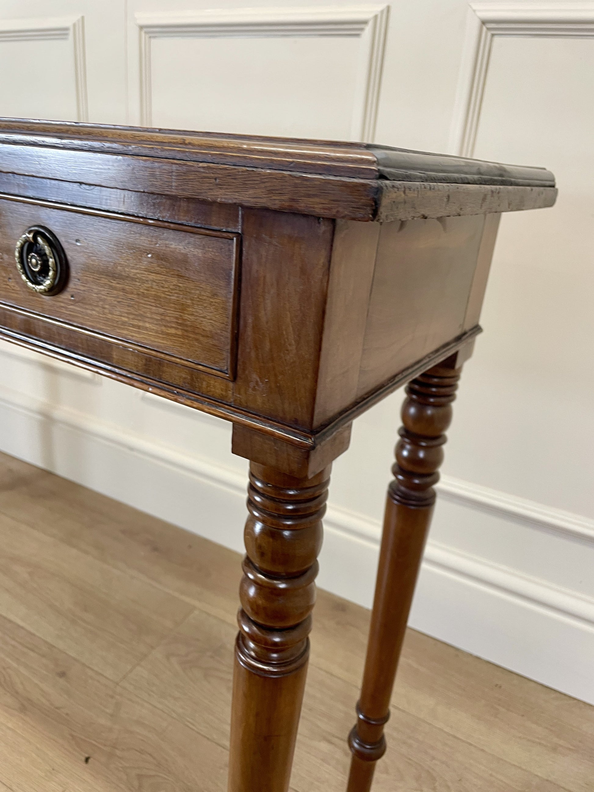 Wooden side table with a single drawer against a white paneled wall.