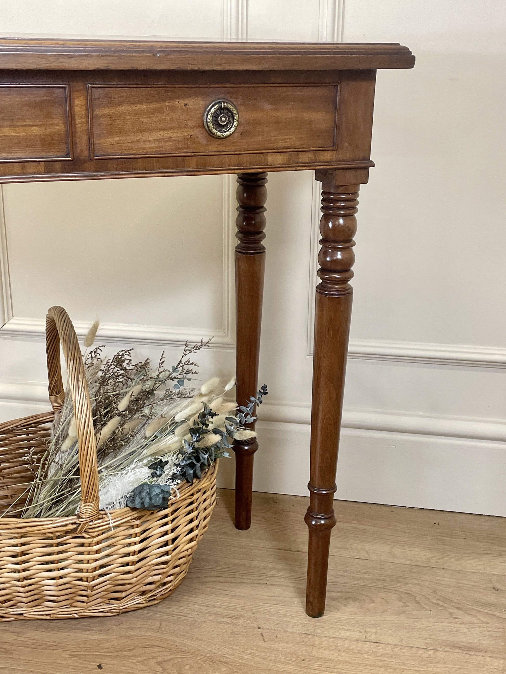 Wooden console table with a basket of dried plants on a wooden floor.