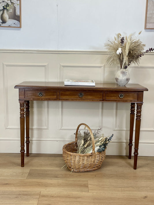 Wooden console table with decorative items against a white wall.