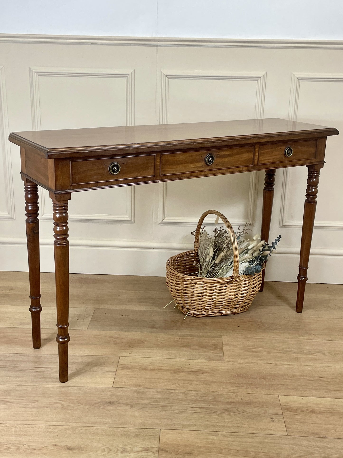 Wooden console table with two drawers against a white paneled wall.