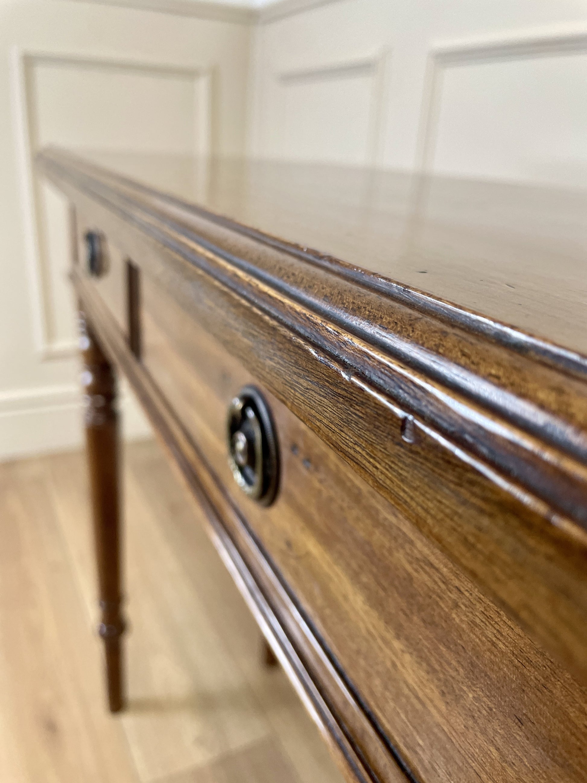 Wooden table with metal handles against a white paneled wall.