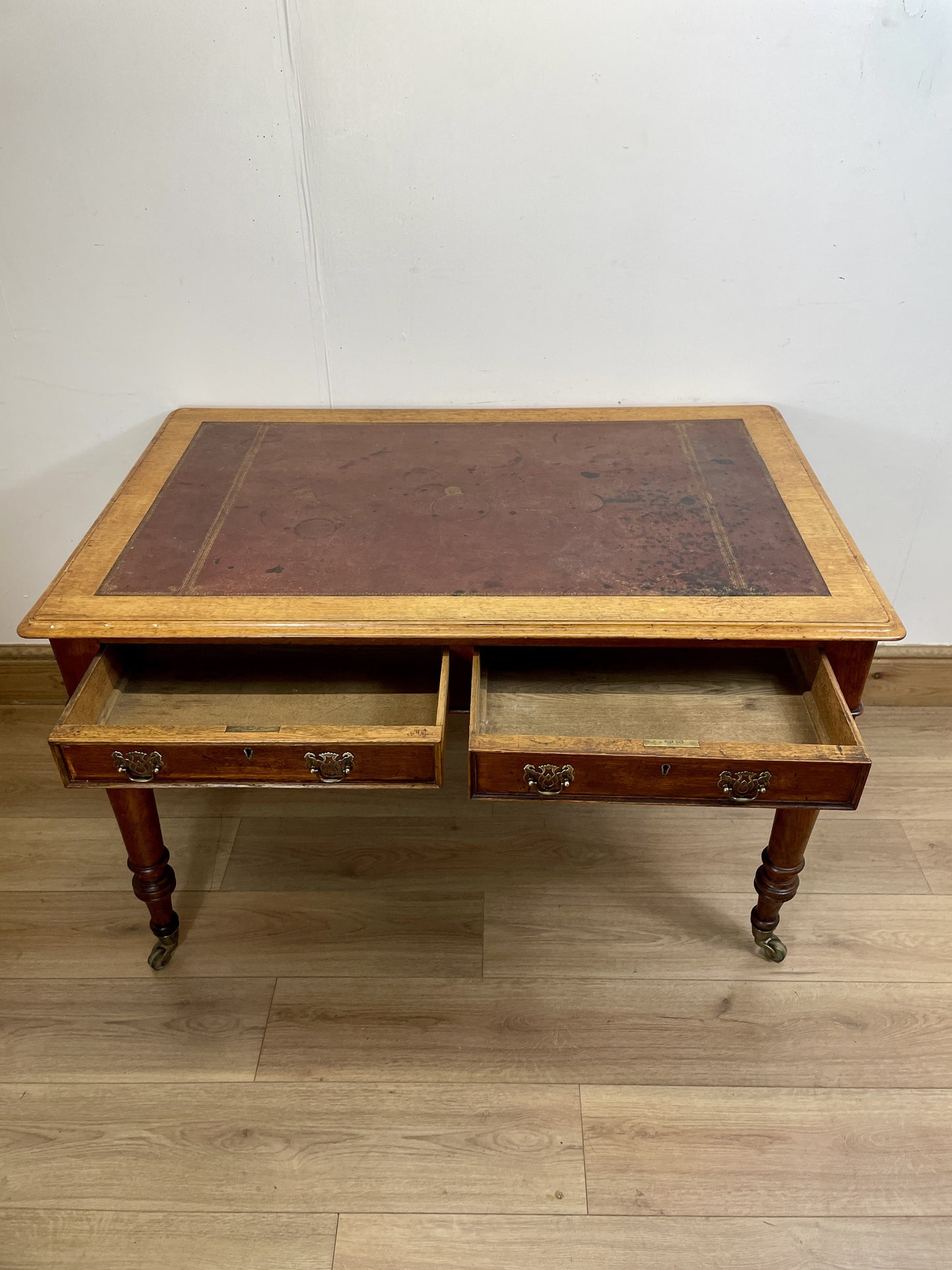 Wooden desk with leather top on a wooden floor against a white wall