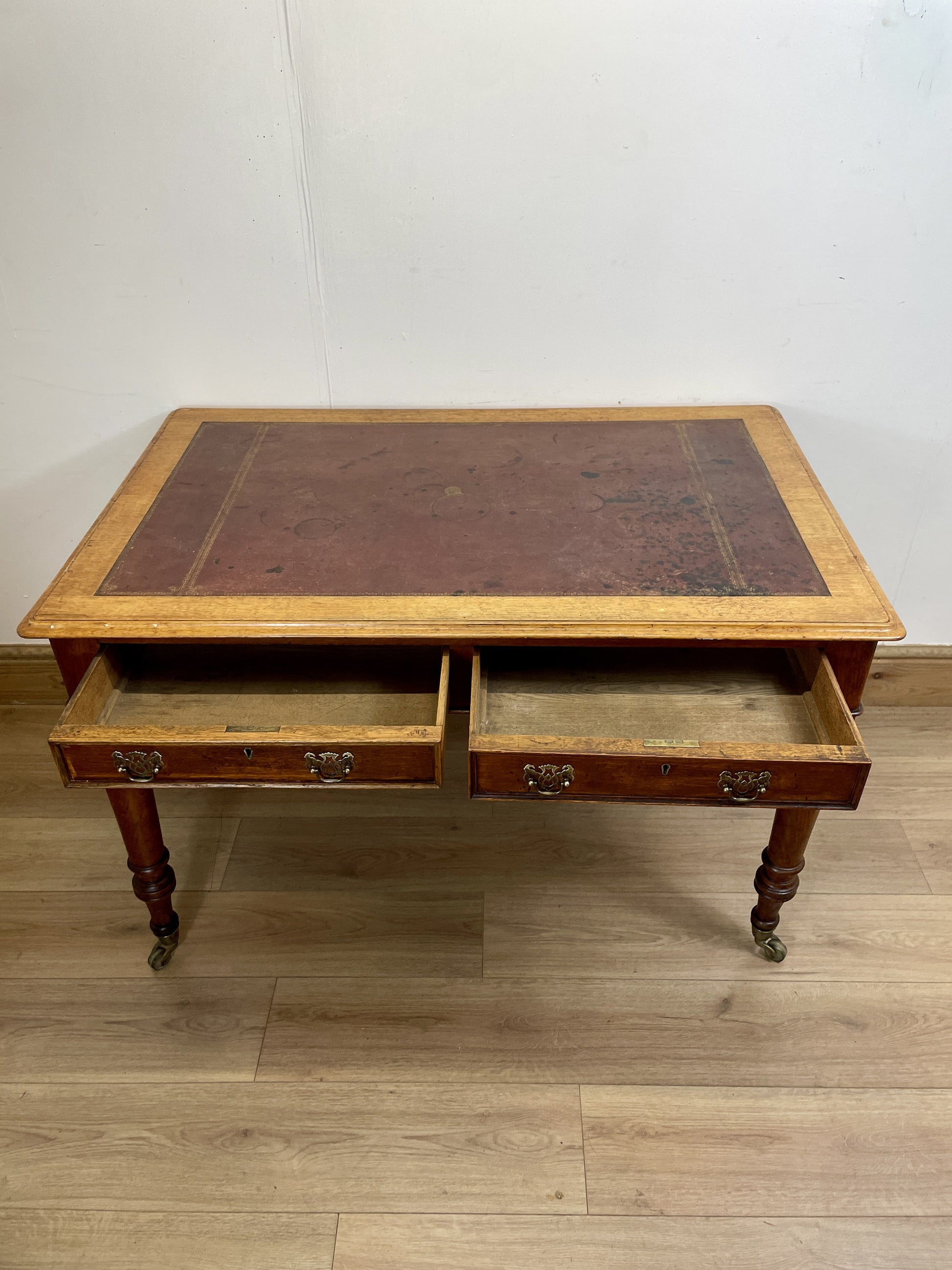 Wooden desk with leather top on a wooden floor against a white wall