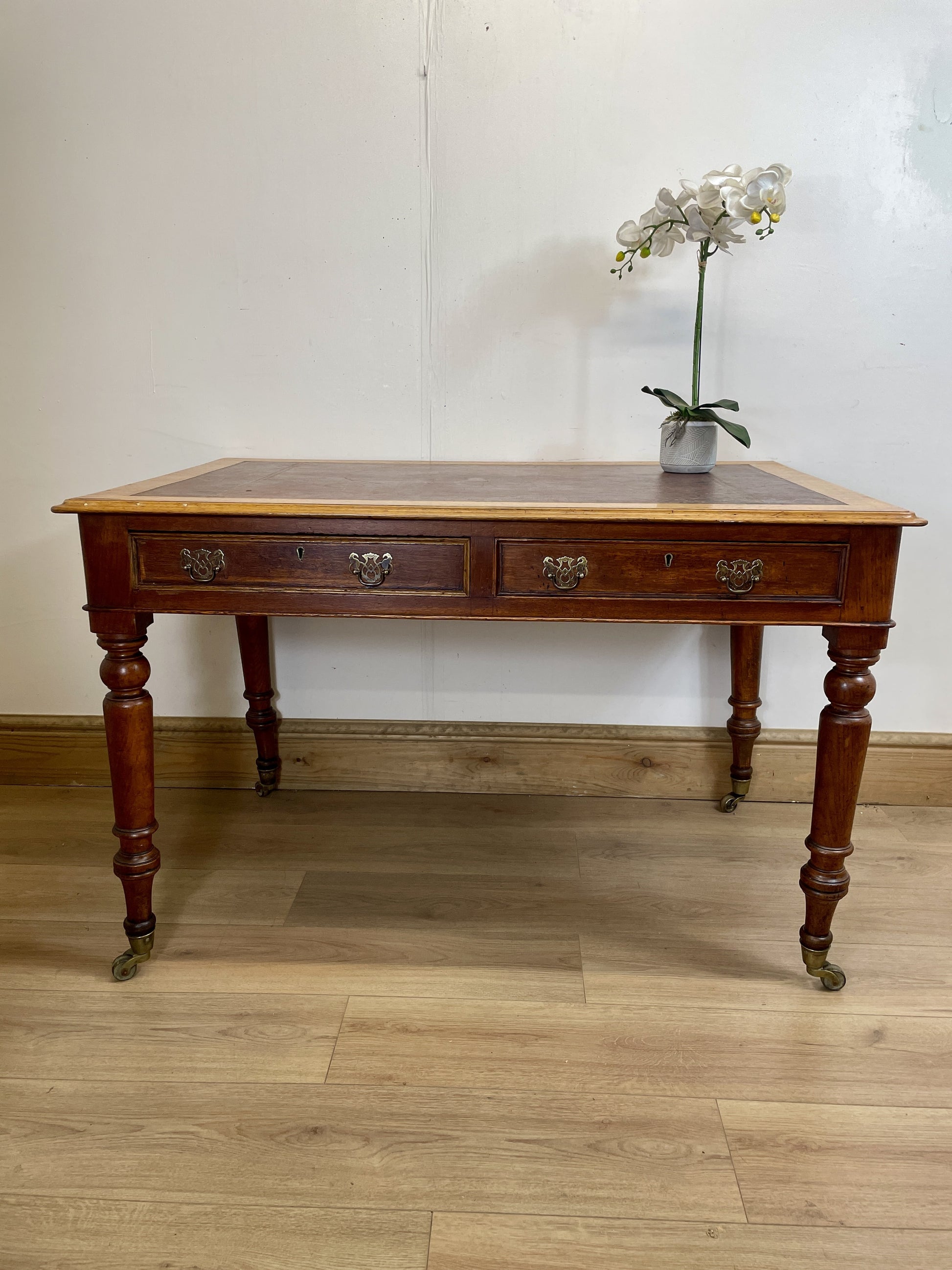 Wooden desk with a vase of flowers on a wooden floor.