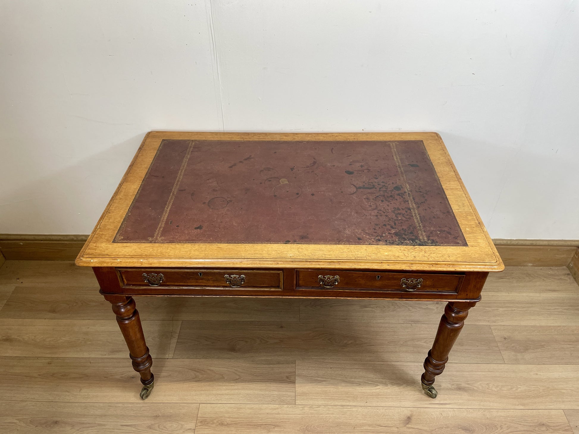 Wooden desk with leather top on a wooden floor against a white wall