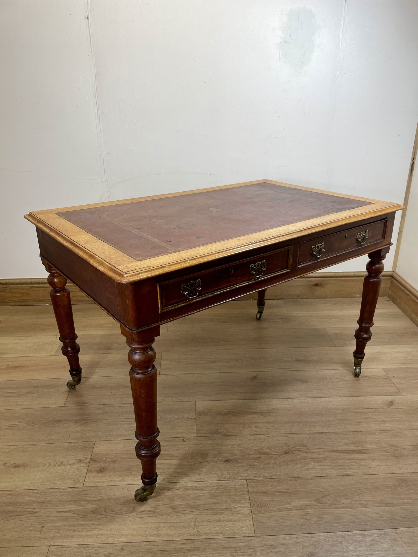 Wooden desk with leather top on a wooden floor against a white wall