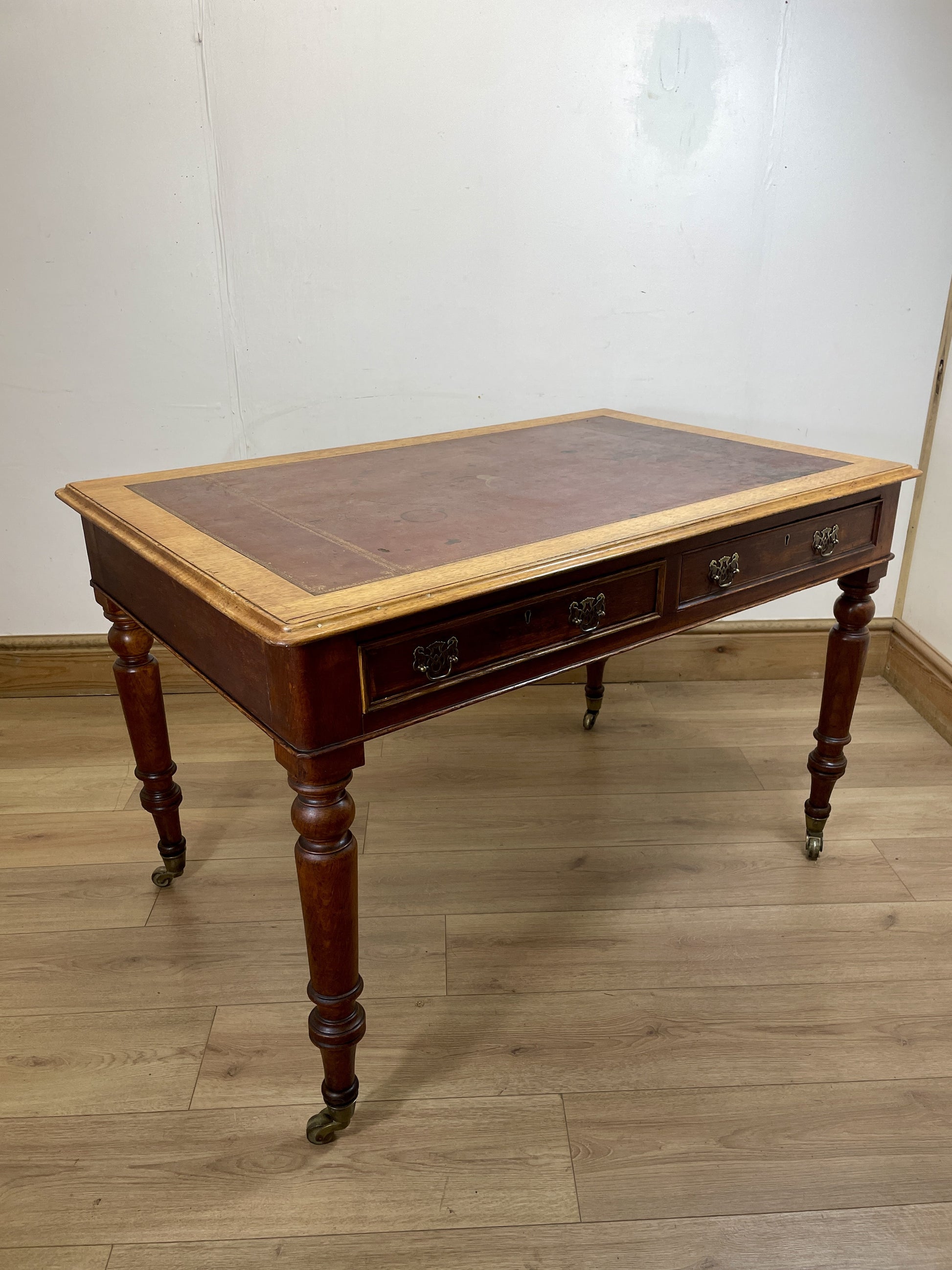 Wooden desk with leather top on a wooden floor against a white wall