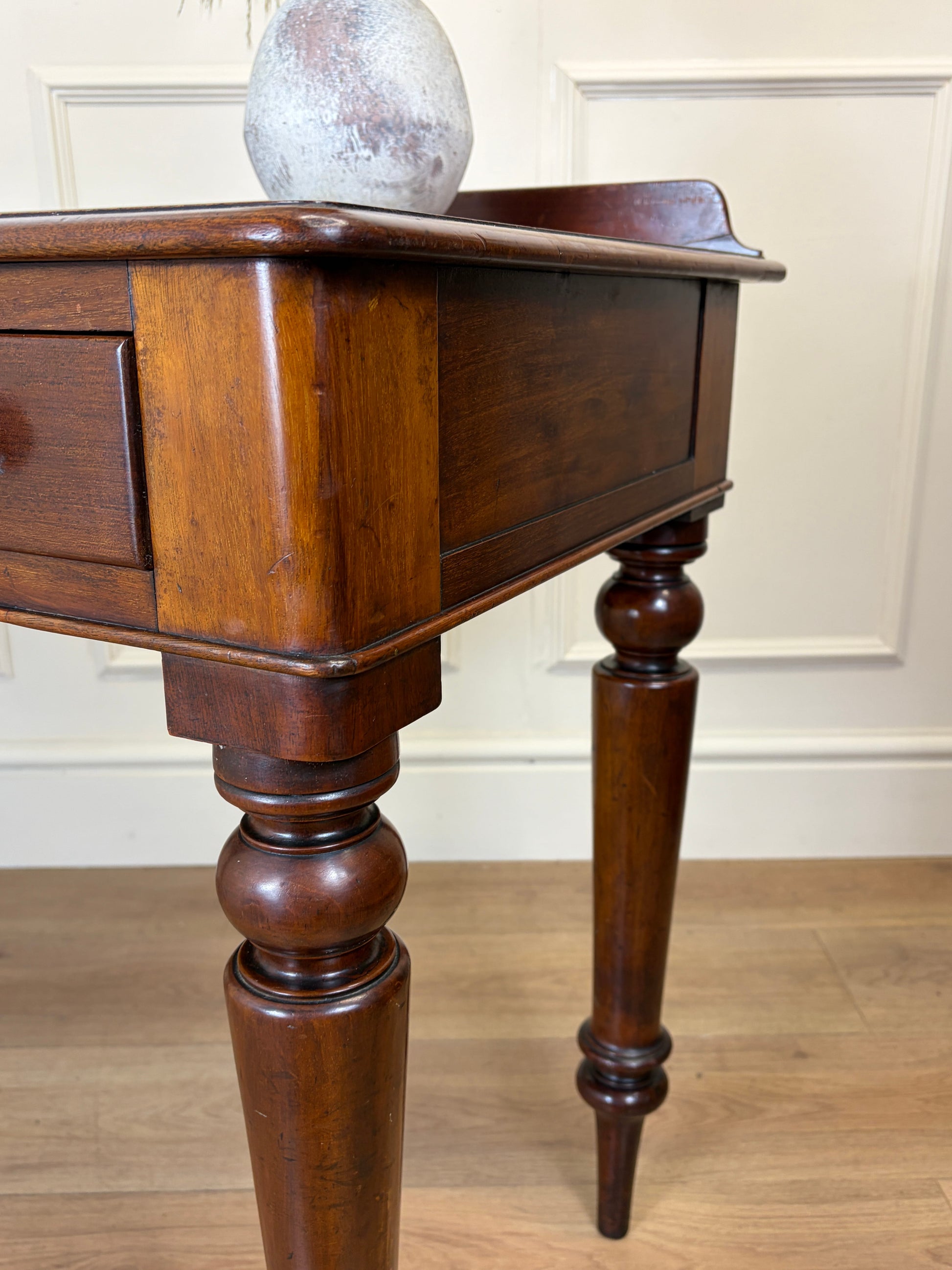 Wooden side table with a spherical object on top against a white wall.