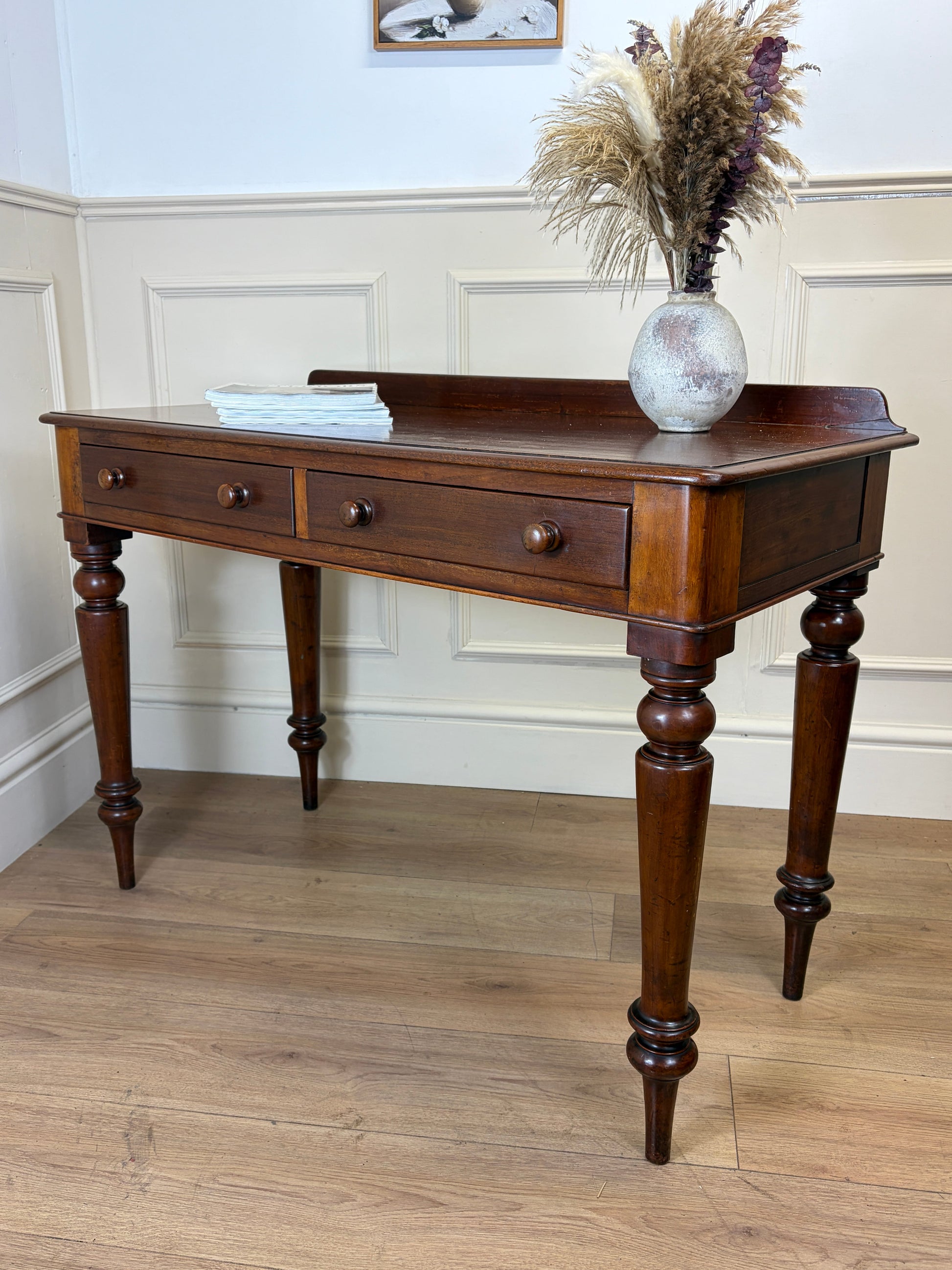 Wooden console table with a vase of dried flowers on a wooden floor.