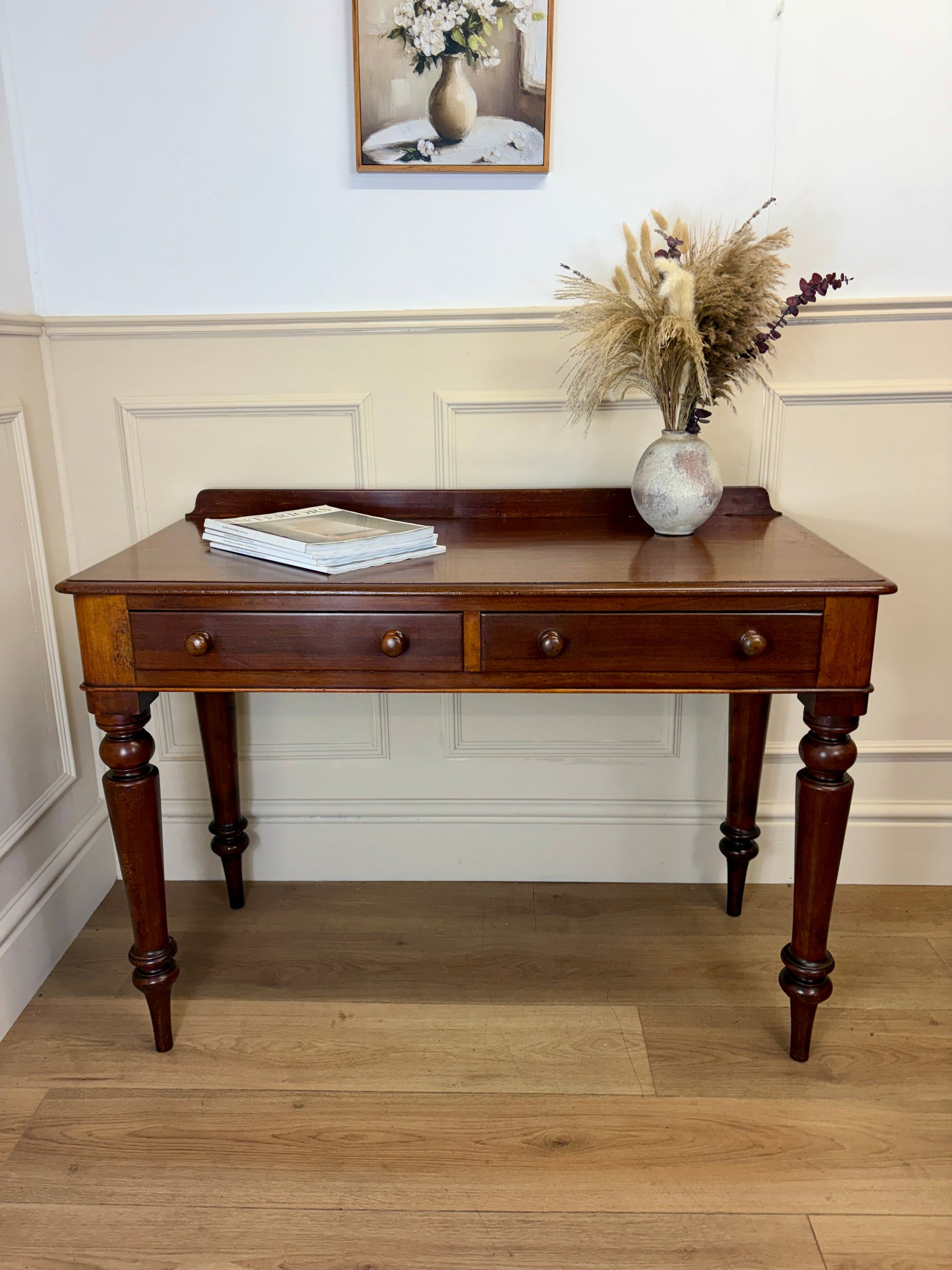 Wooden console table with a vase and books on a wooden floor.