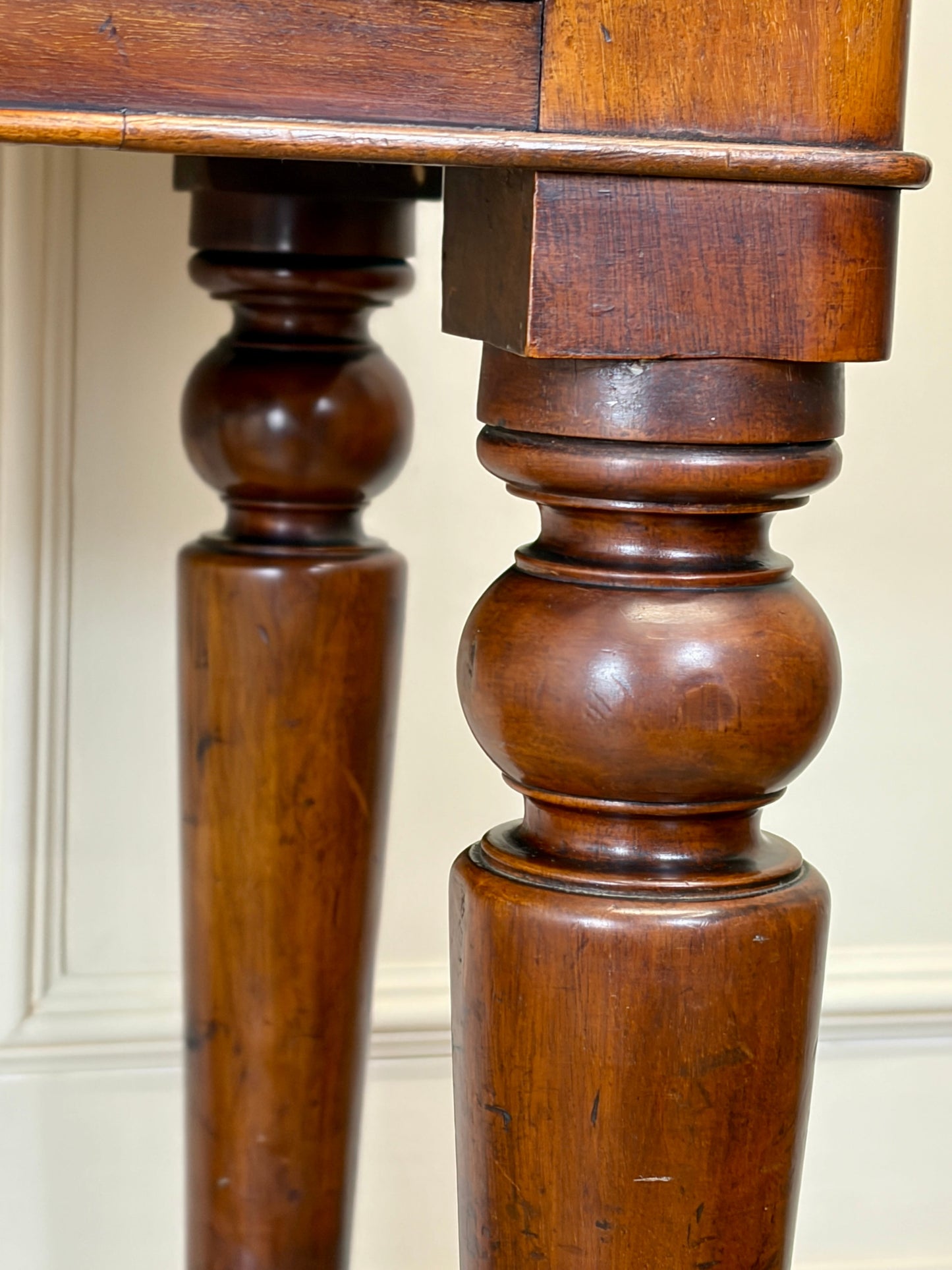 Close-up of a wooden table with turned legs against a neutral background