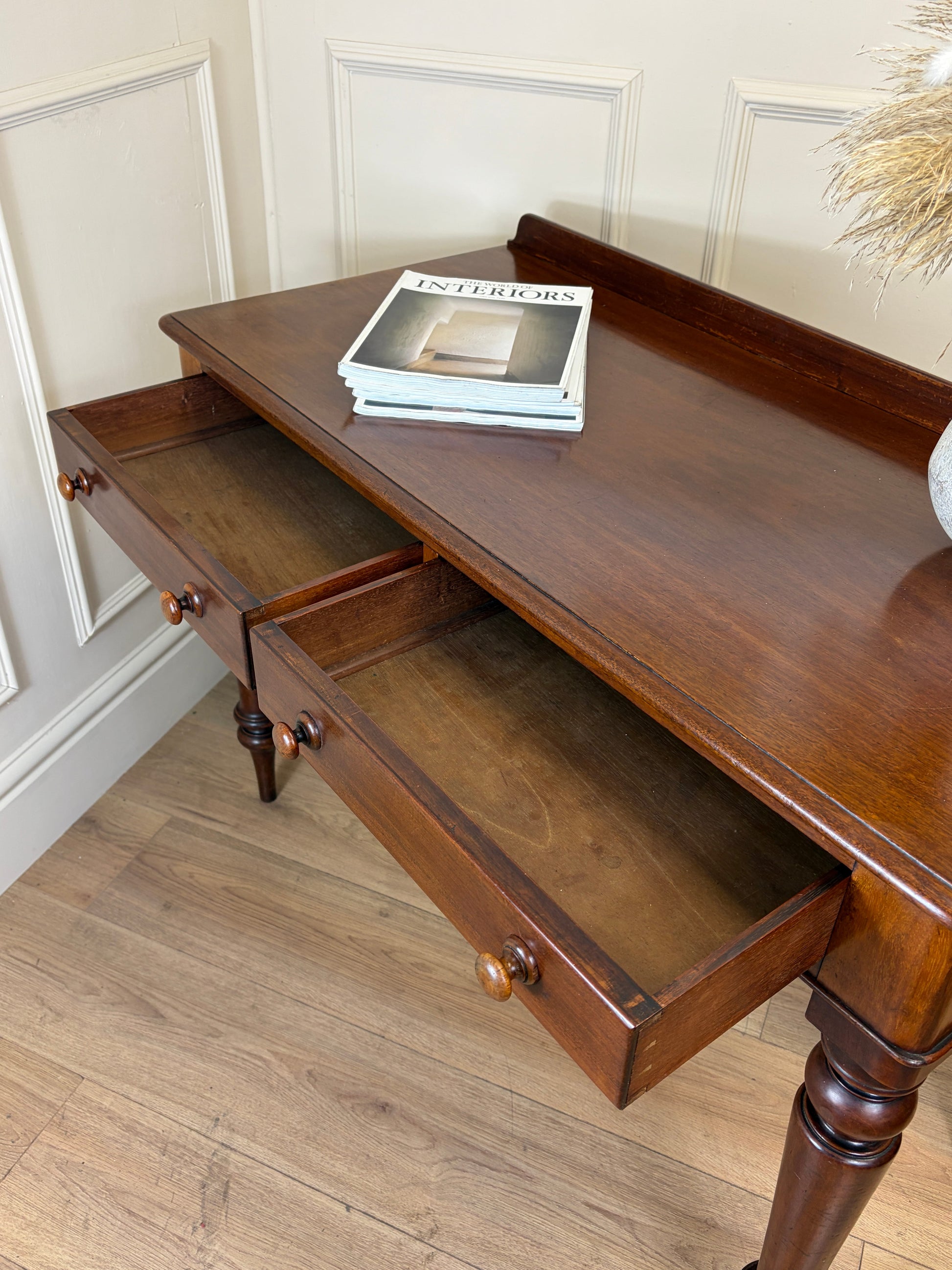 Wooden side table with a drawer and books on top against a white paneled wall.